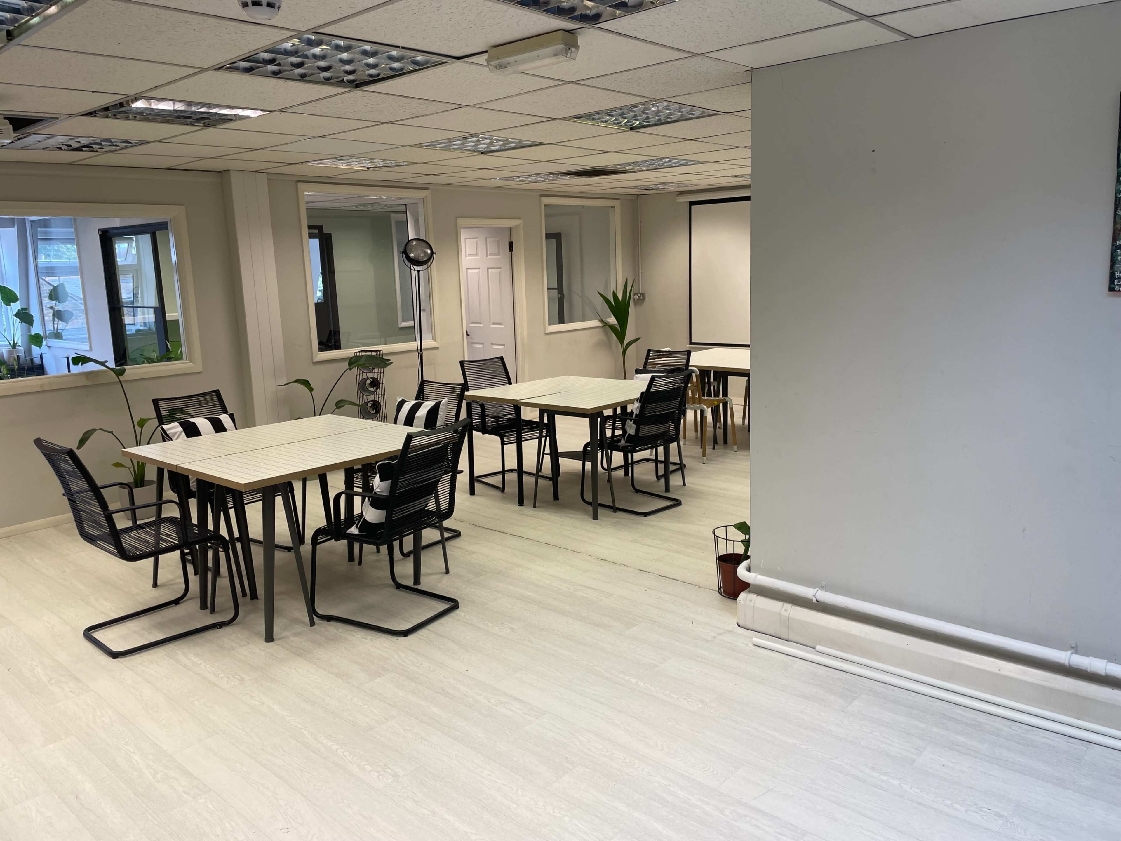 A brightly lit office space with several tables and chairs arranged neatly in a room with windows and plants.