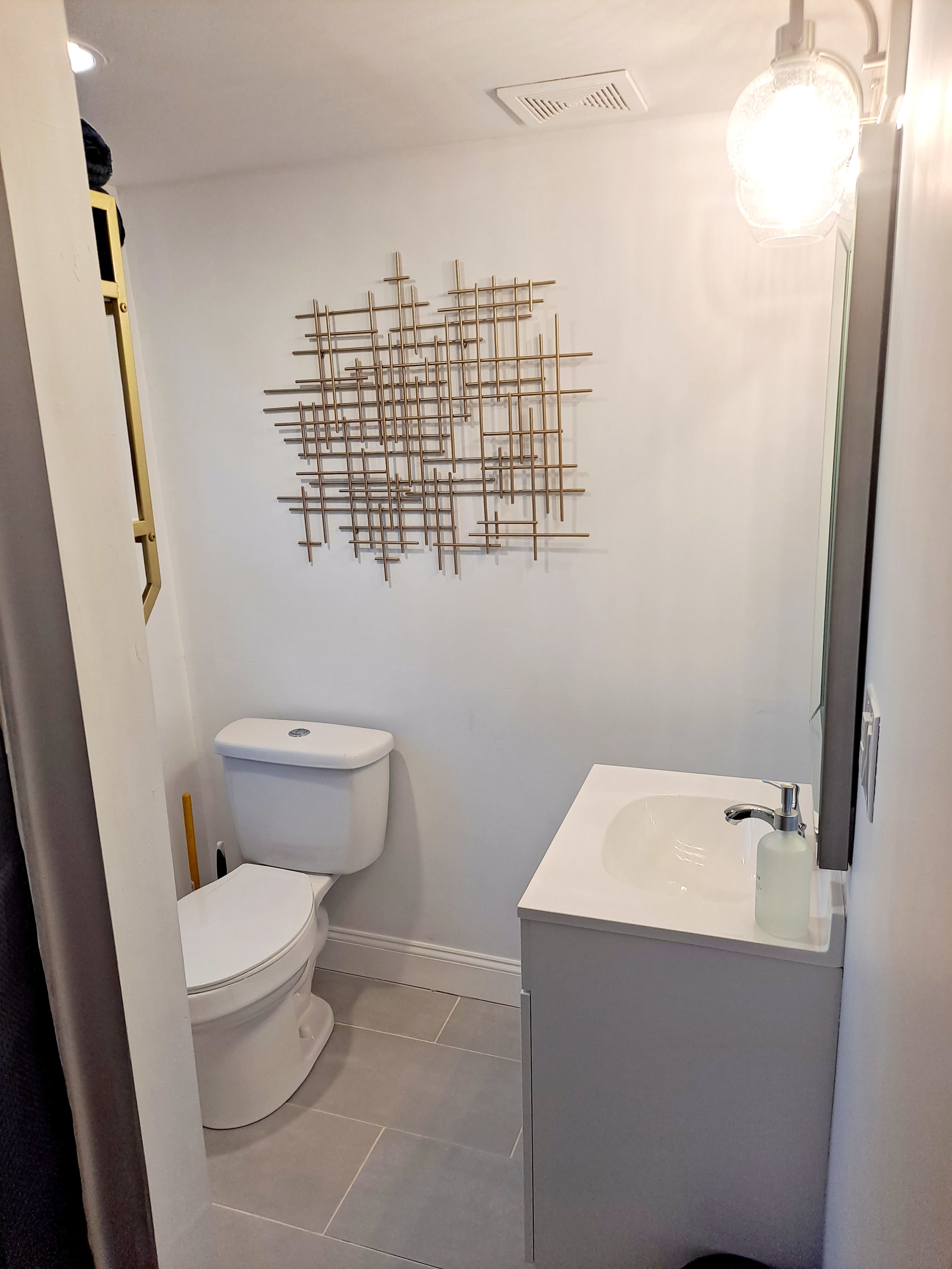 A modern bathroom features a toilet, a sleek vanity with a sink, and a decorative wall hanging made of intersecting lines.