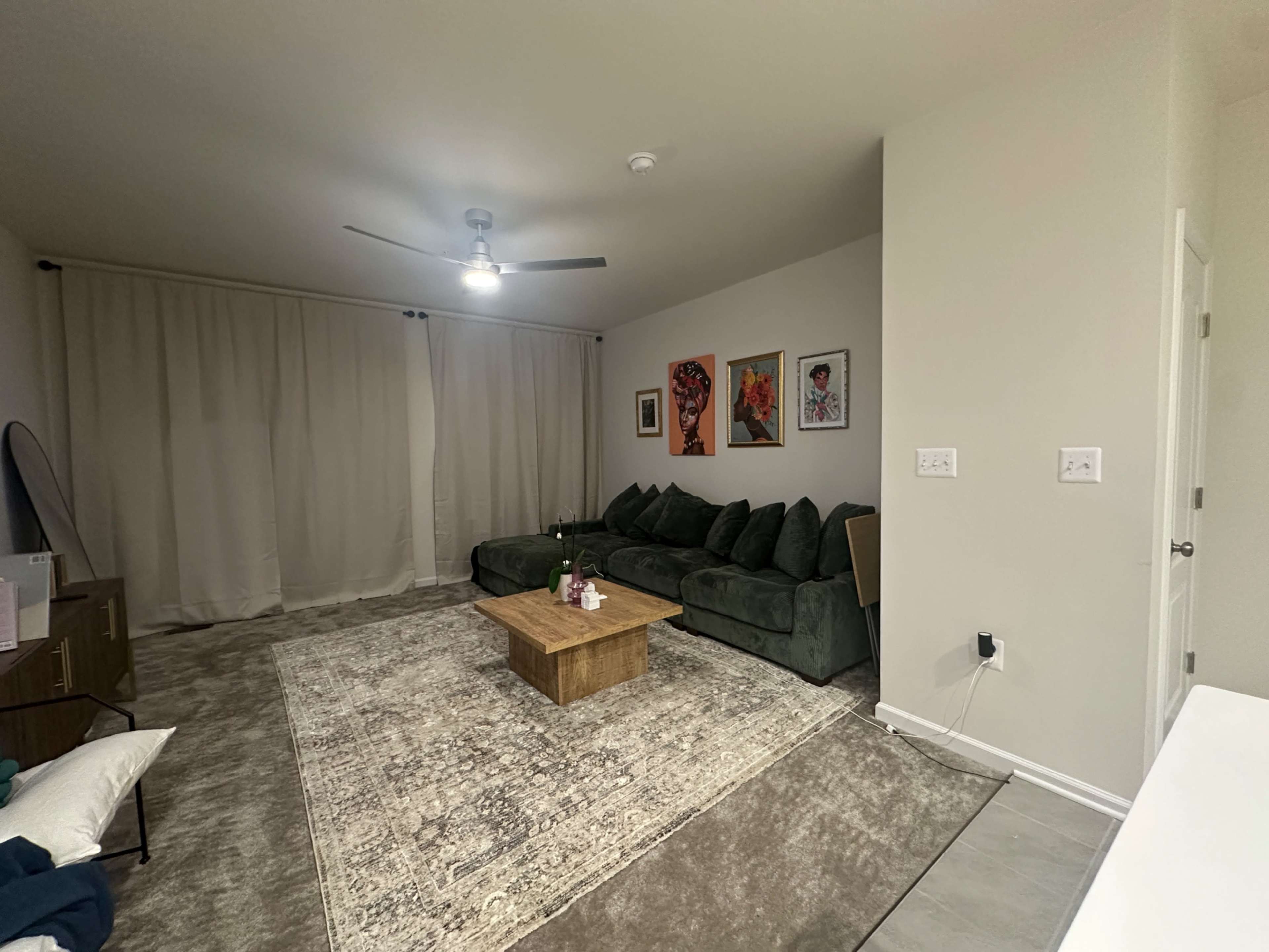 The image shows a modern living room with a dark green sectional sofa, a wooden coffee table, and abstract wall art.
