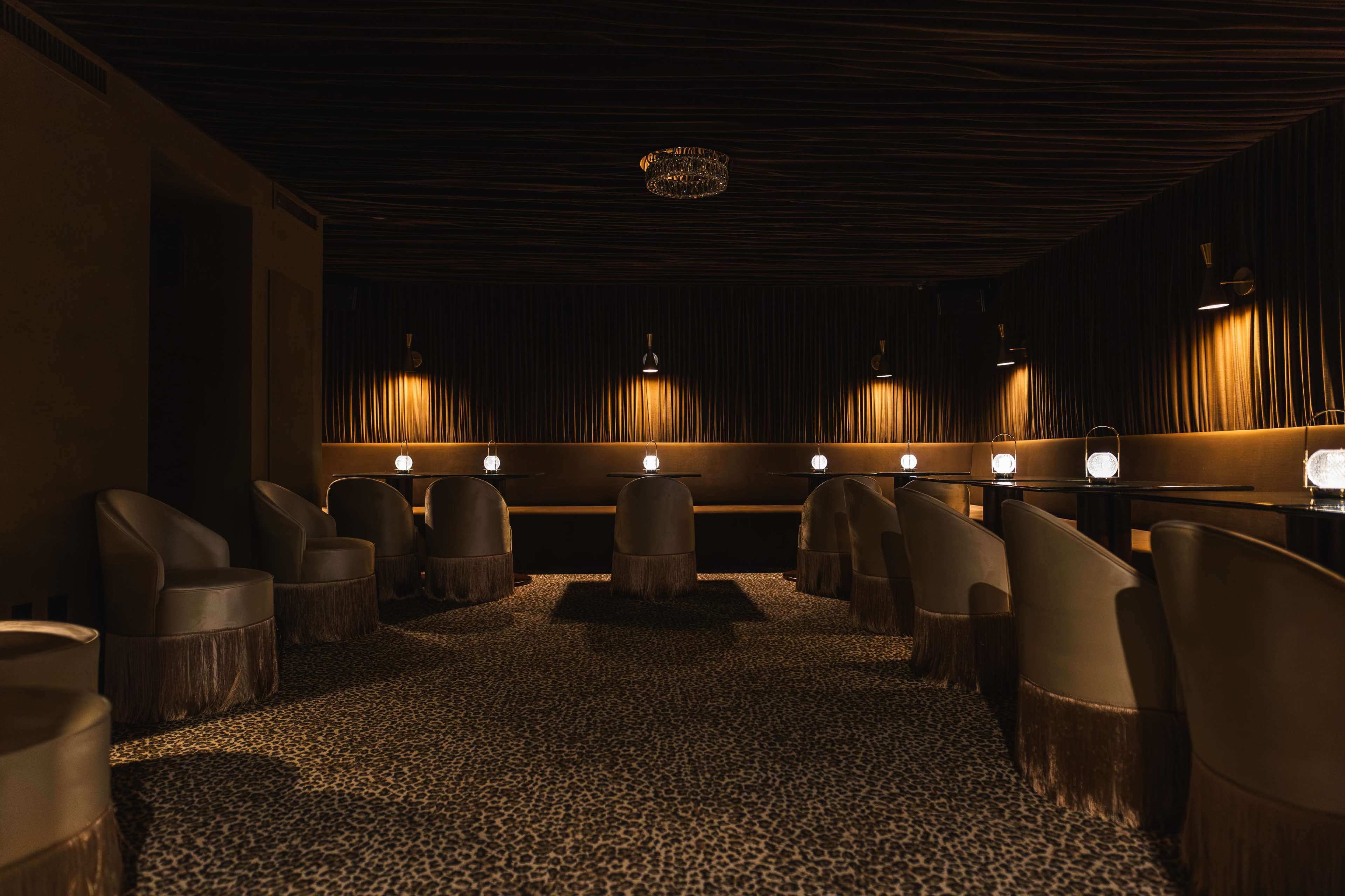 A dimly lit lounge features circular chairs arranged in a semicircle around small tables, with soft lighting creating a cozy atmosphere.