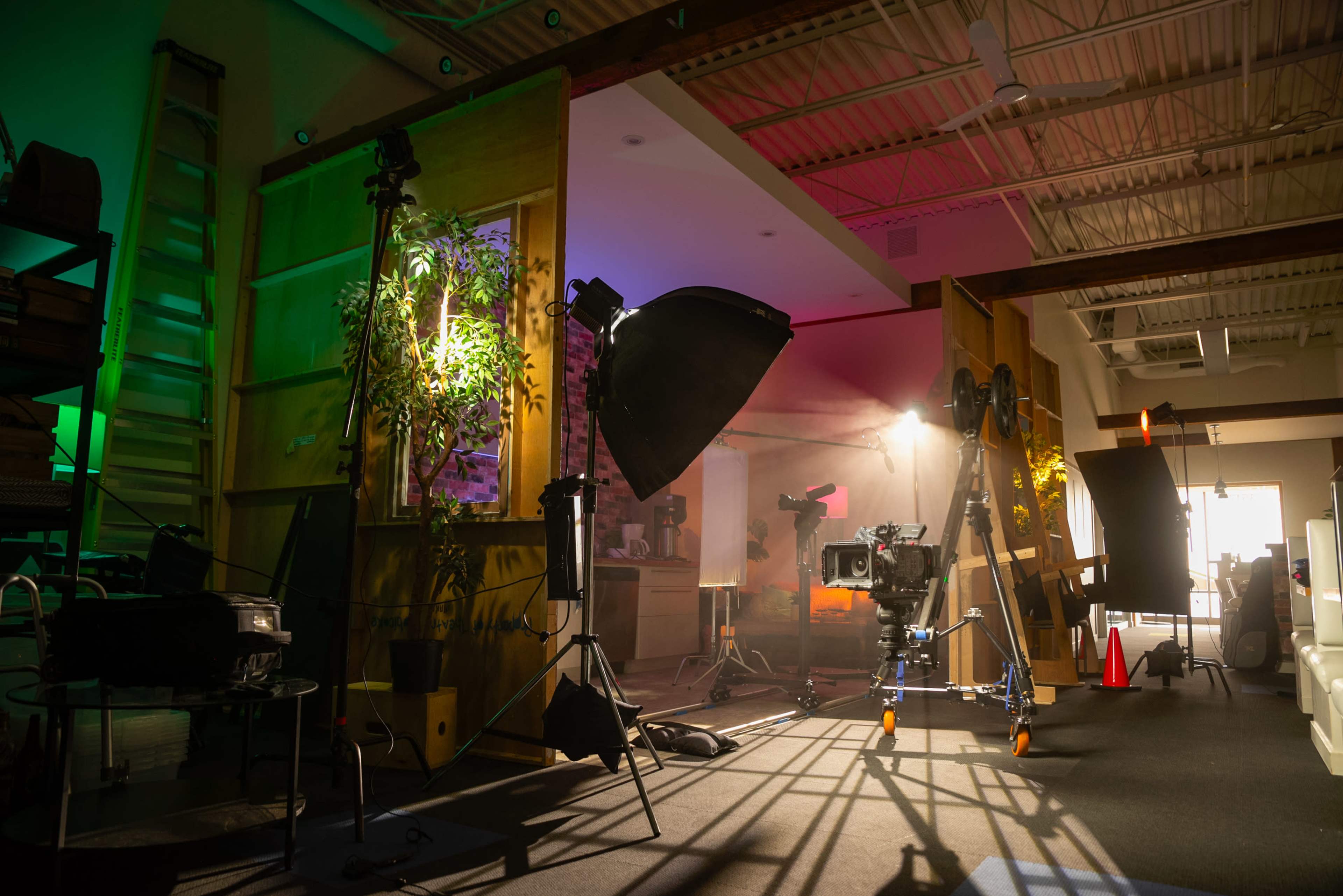 A photography studio setup with various lighting equipment, cameras on tripods, and a backdrop illuminated by colorful lights.