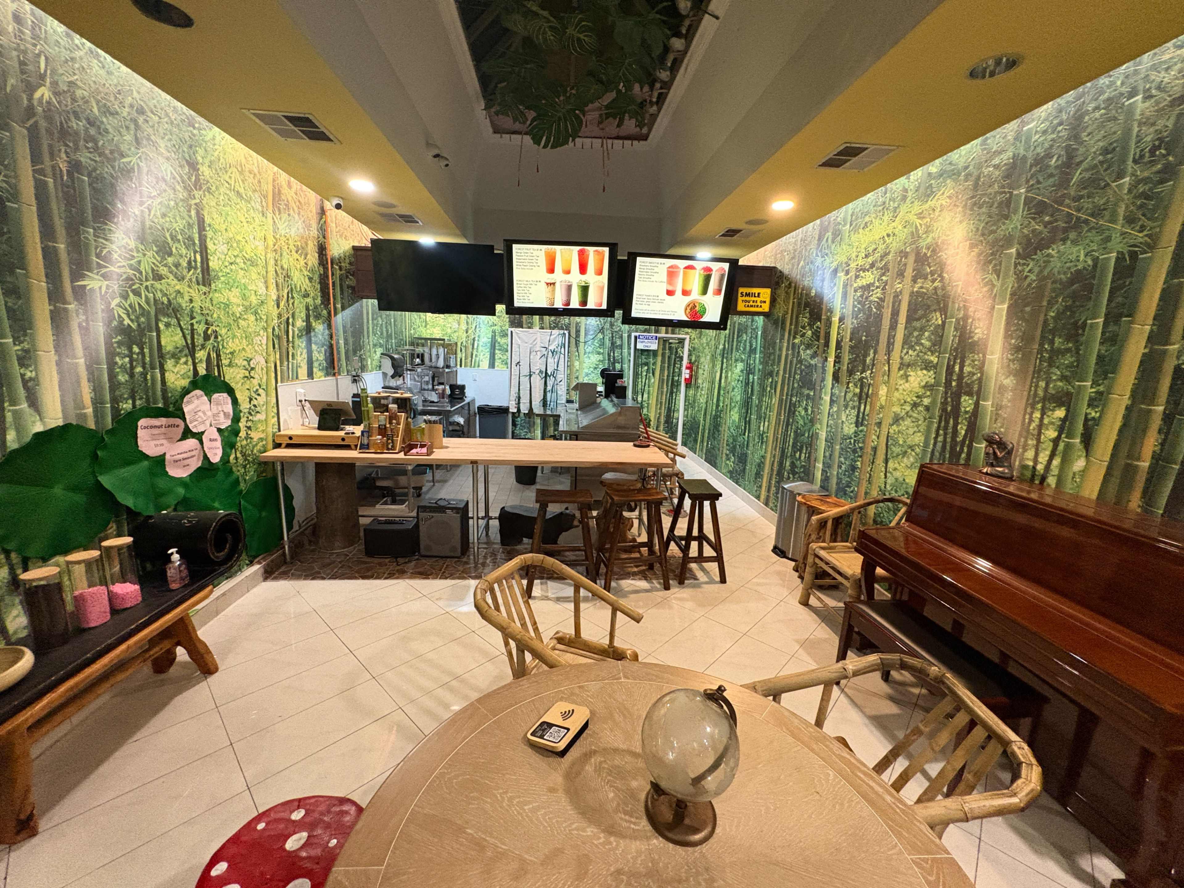 The image shows a café interior decorated with bamboo-themed wallpaper, featuring a counter with seating and a piano.