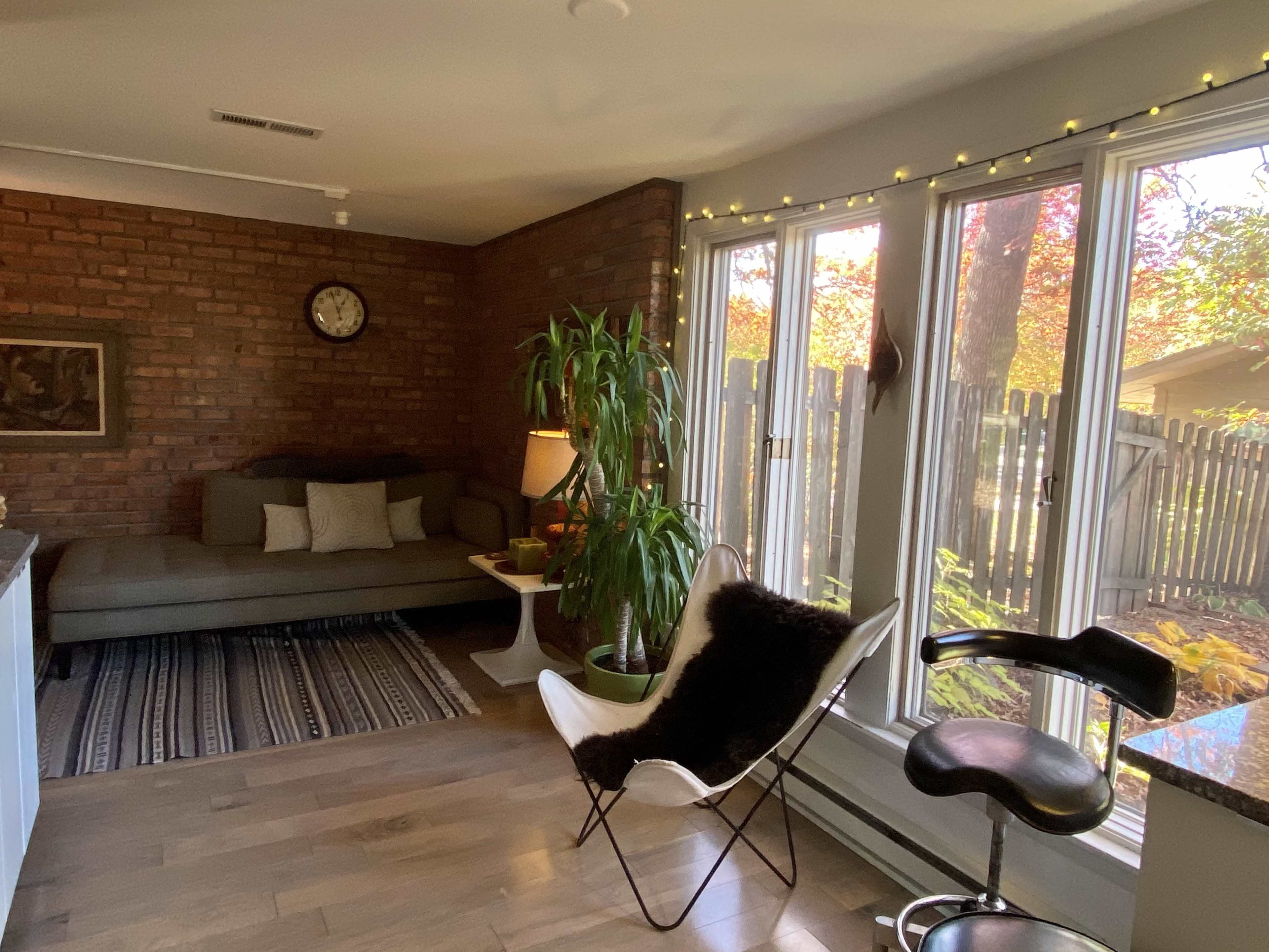 A cozy sitting area with a brick wall, large windows featuring natural light, and a mix of modern and vintage furniture.