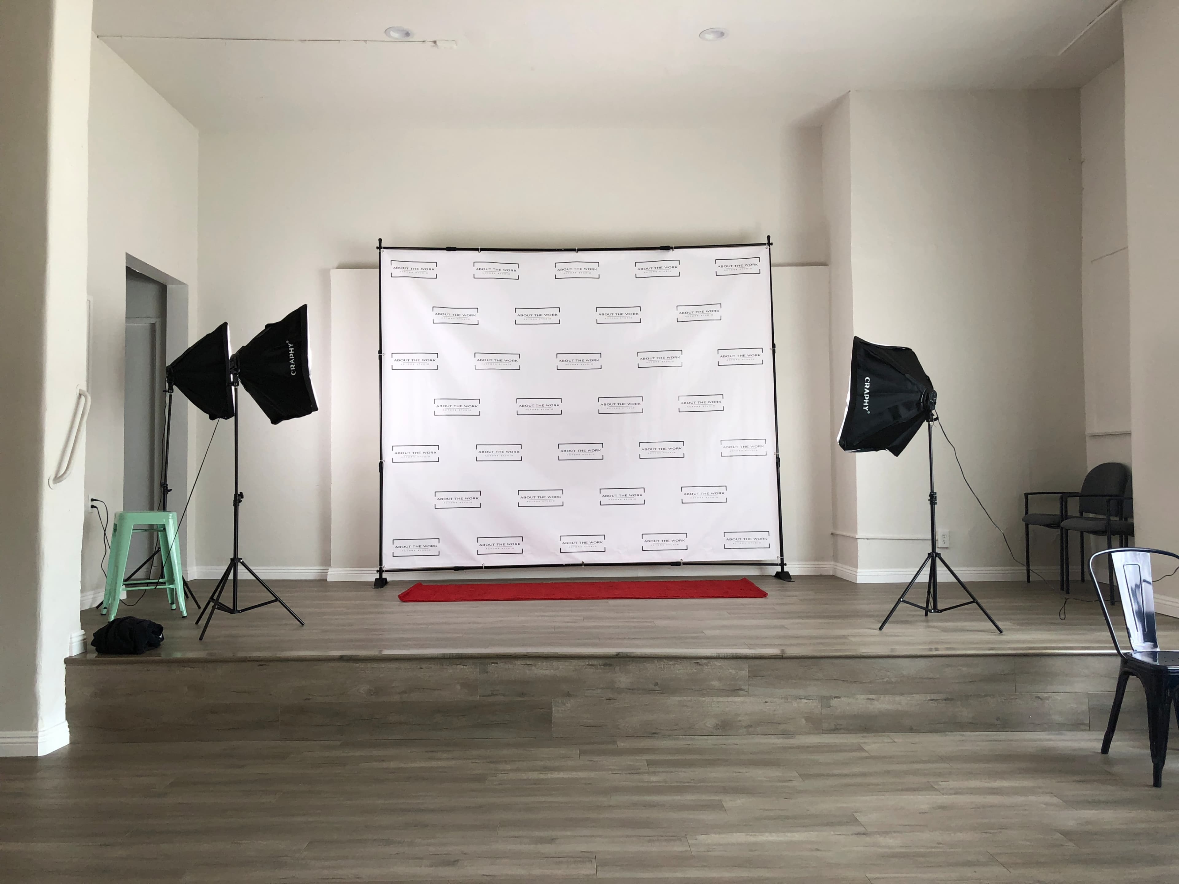 A stage area with a white backdrop, two lighting setups on either side, and a red carpet in front.