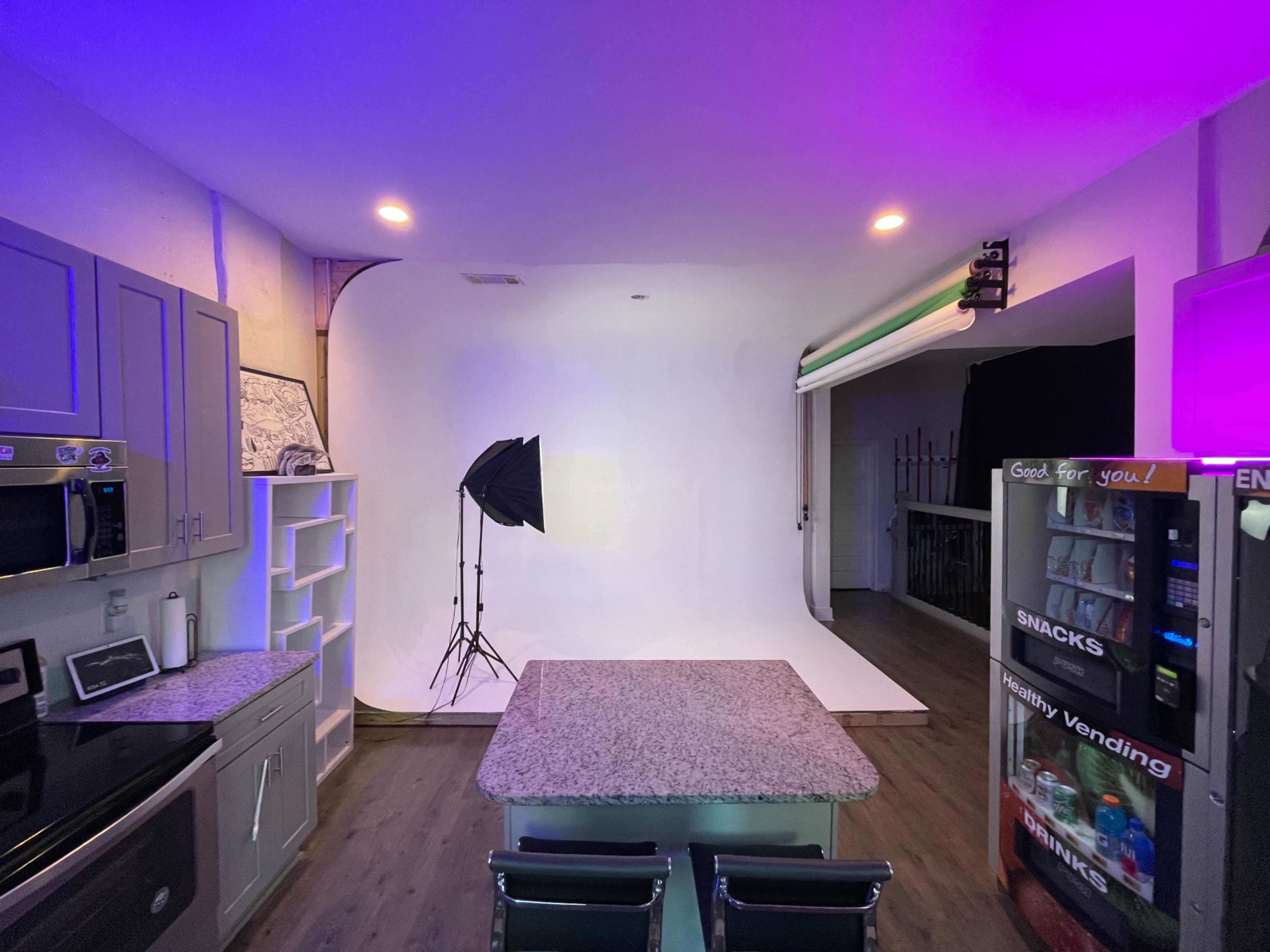 A modern kitchen with a large countertop, a photography backdrop and lighting setup, and a vending machine in the corner.