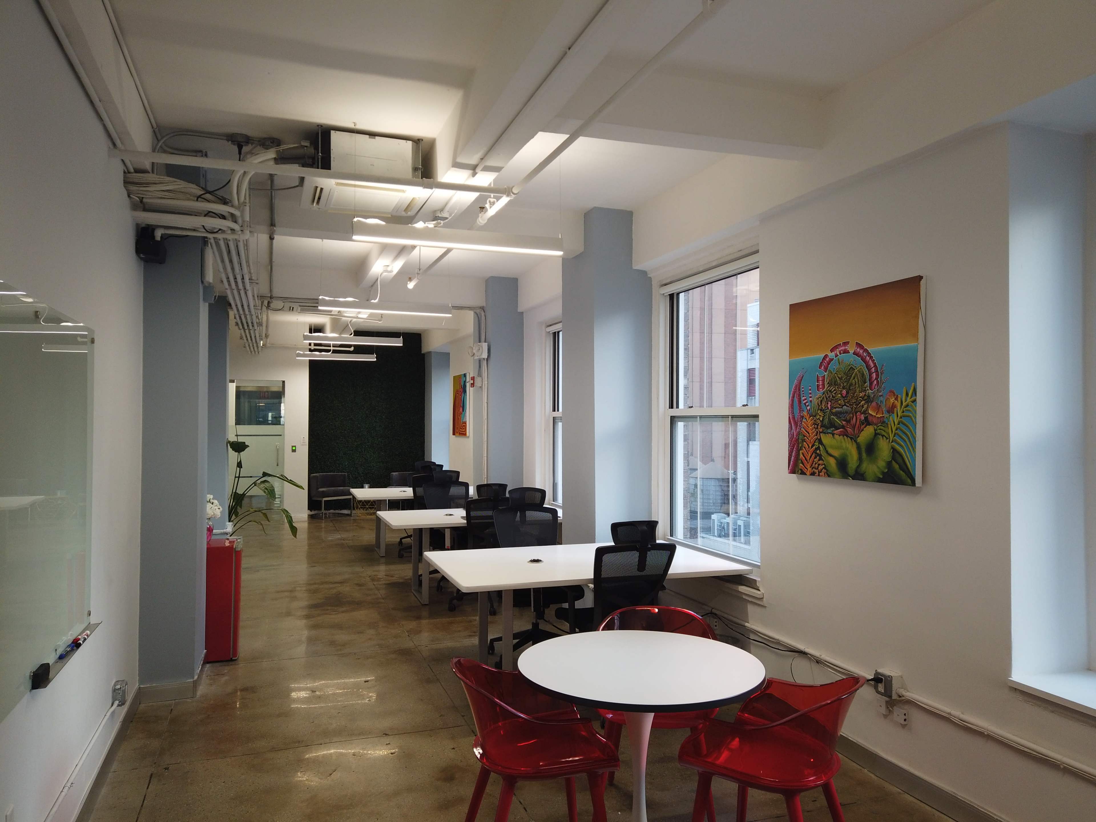 The image shows a modern office space with white tables, black chairs, and colorful wall art, illuminated by overhead lighting.
