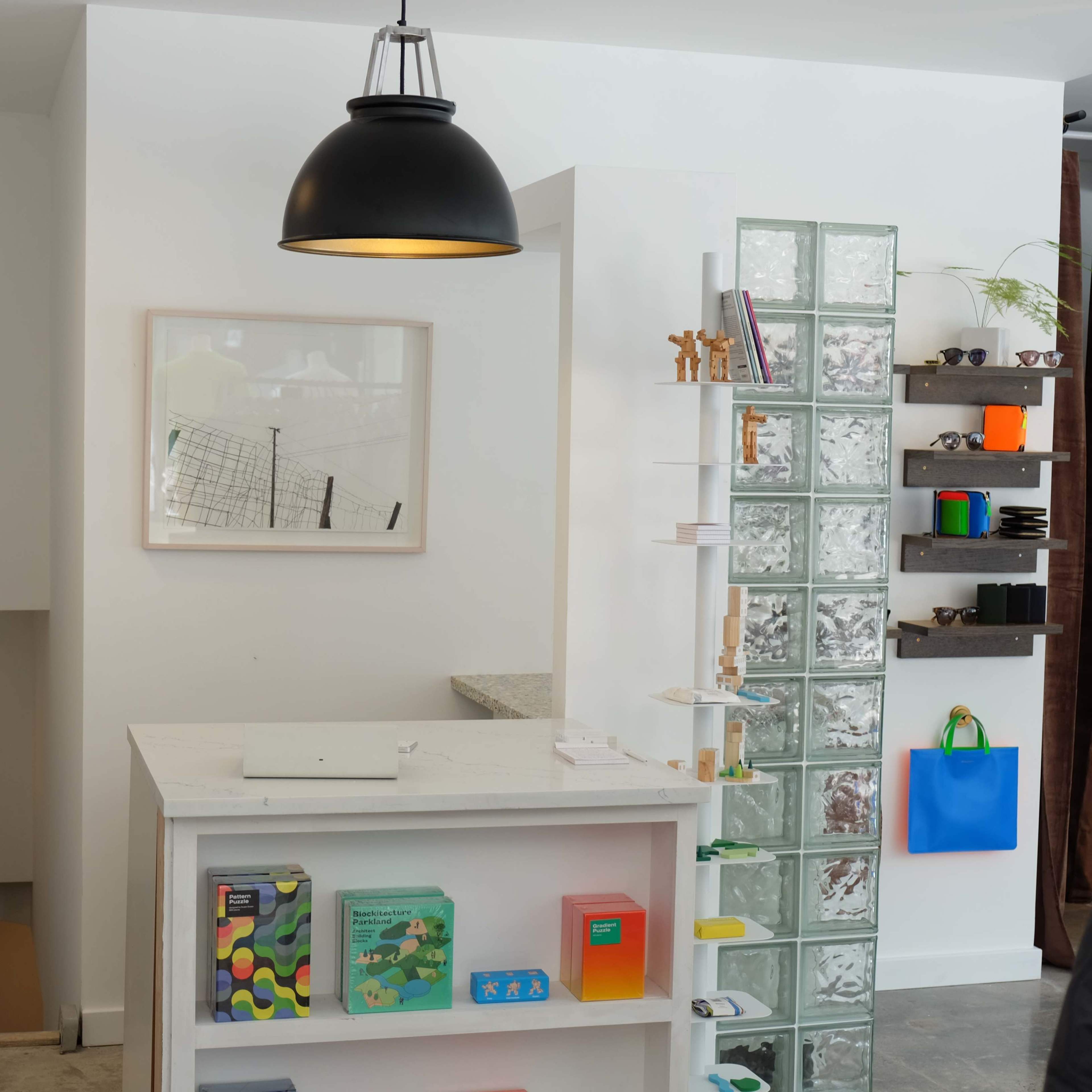 The image shows a modern retail space featuring a display counter, a glass block wall, and shelves with various colorful items.