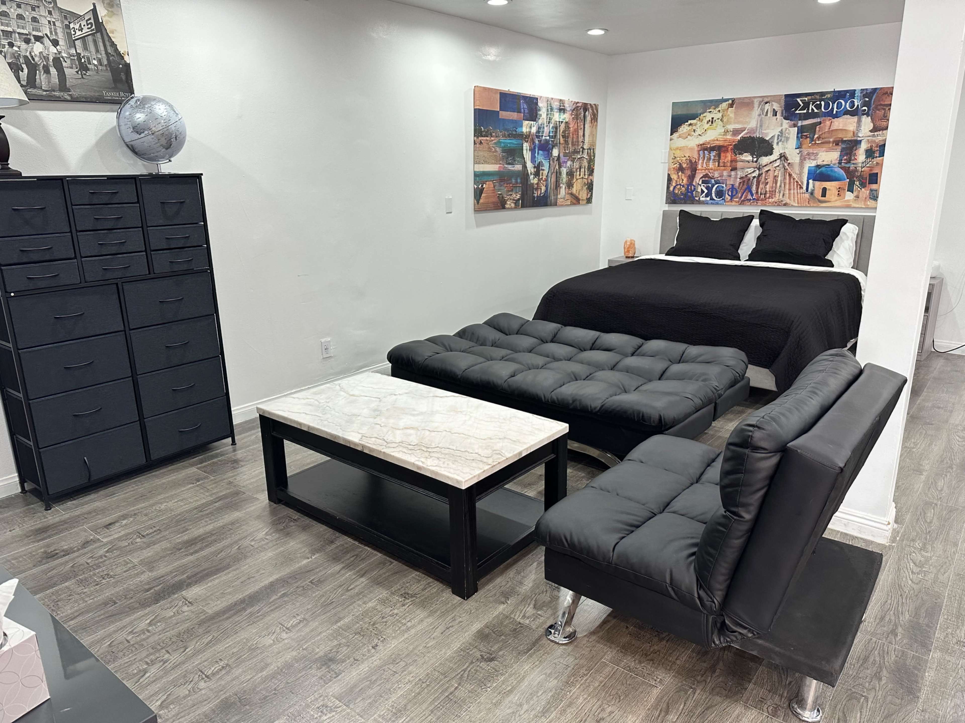 The image shows a small living space with a bed, a coffee table, and seating arranged around a modern decor featuring wall art.