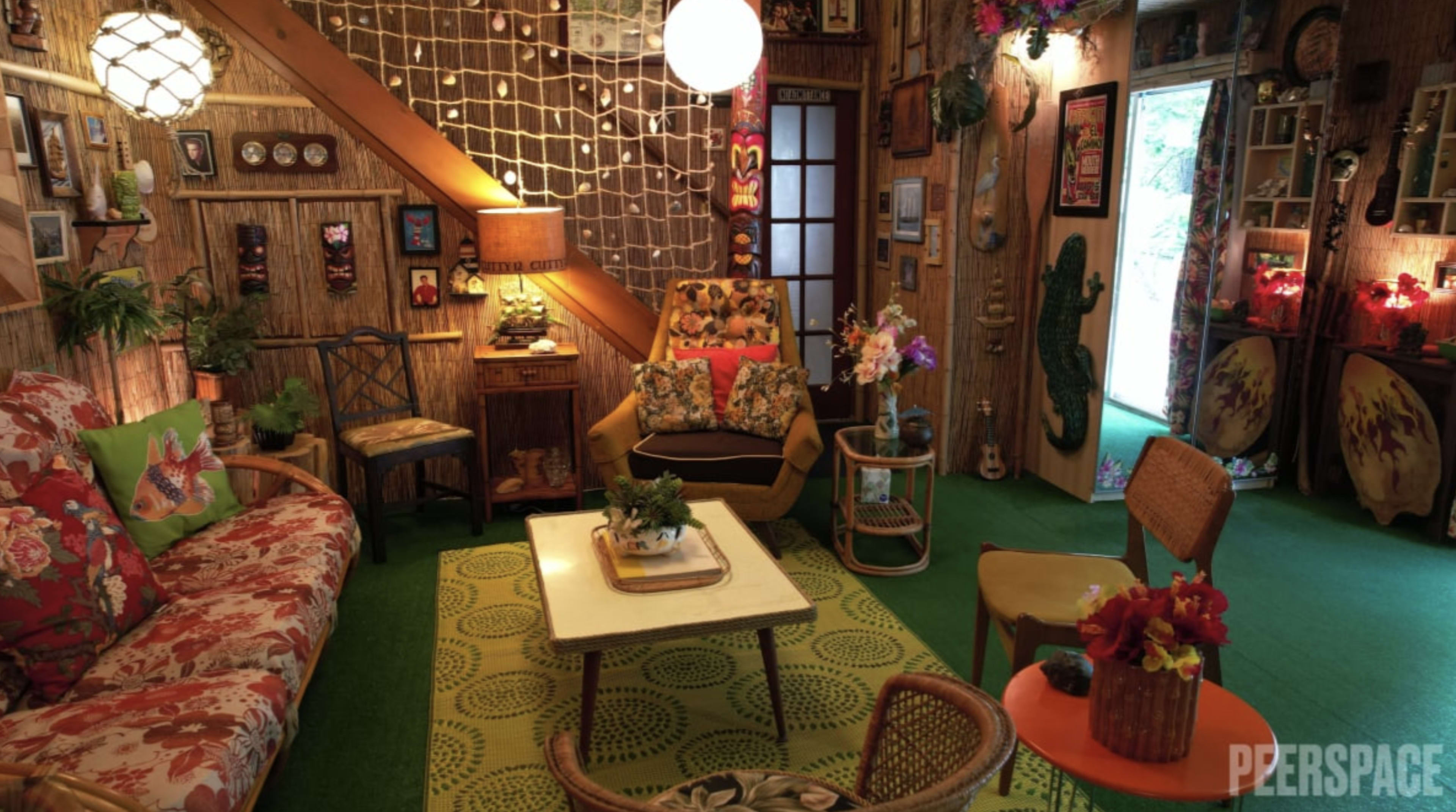 The image shows a cozy living room filled with vintage furniture, colorful floral patterns, and decorative items on the walls.
