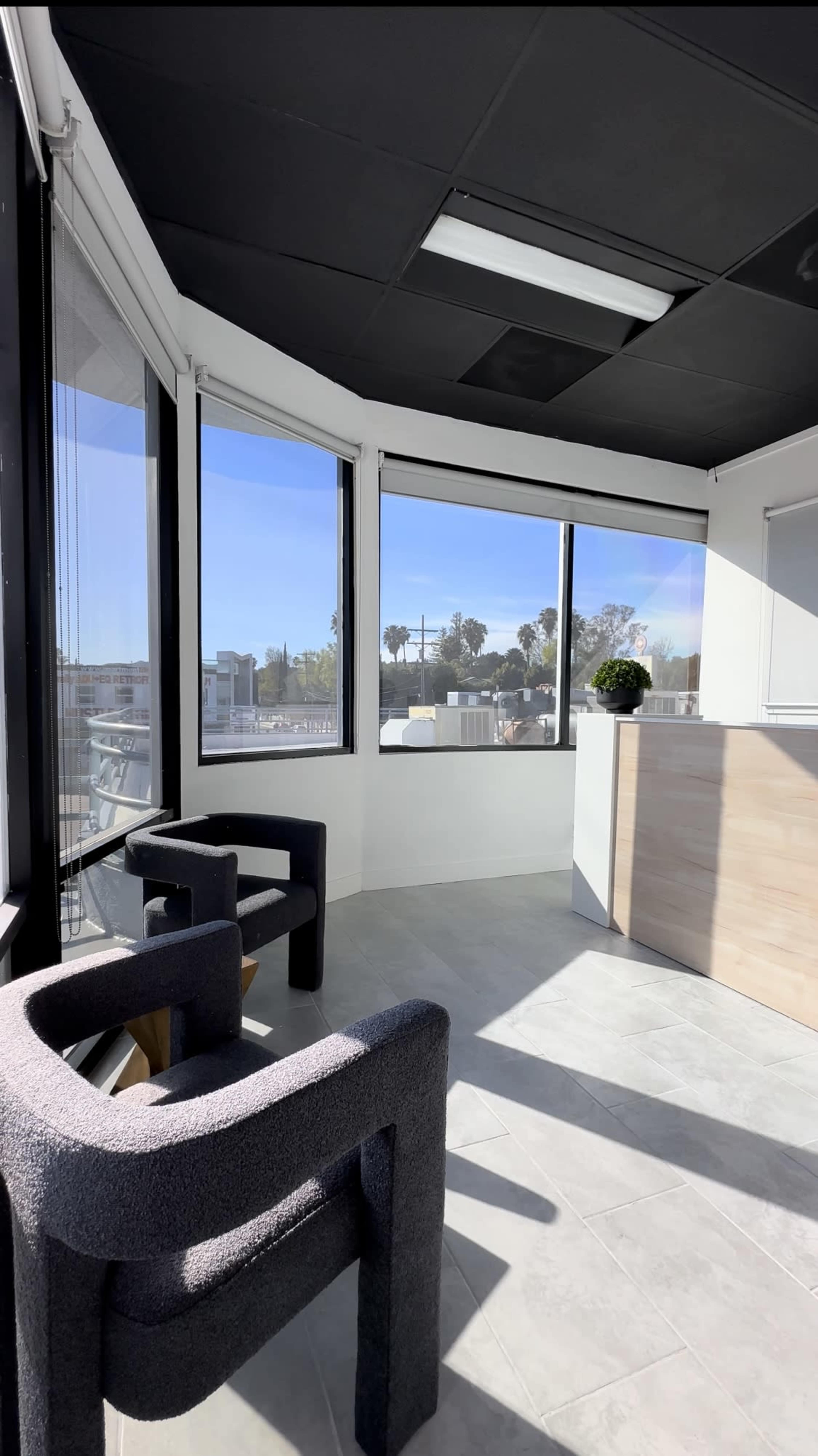 A bright office space featuring a reception desk and two gray armchairs positioned near large windows.