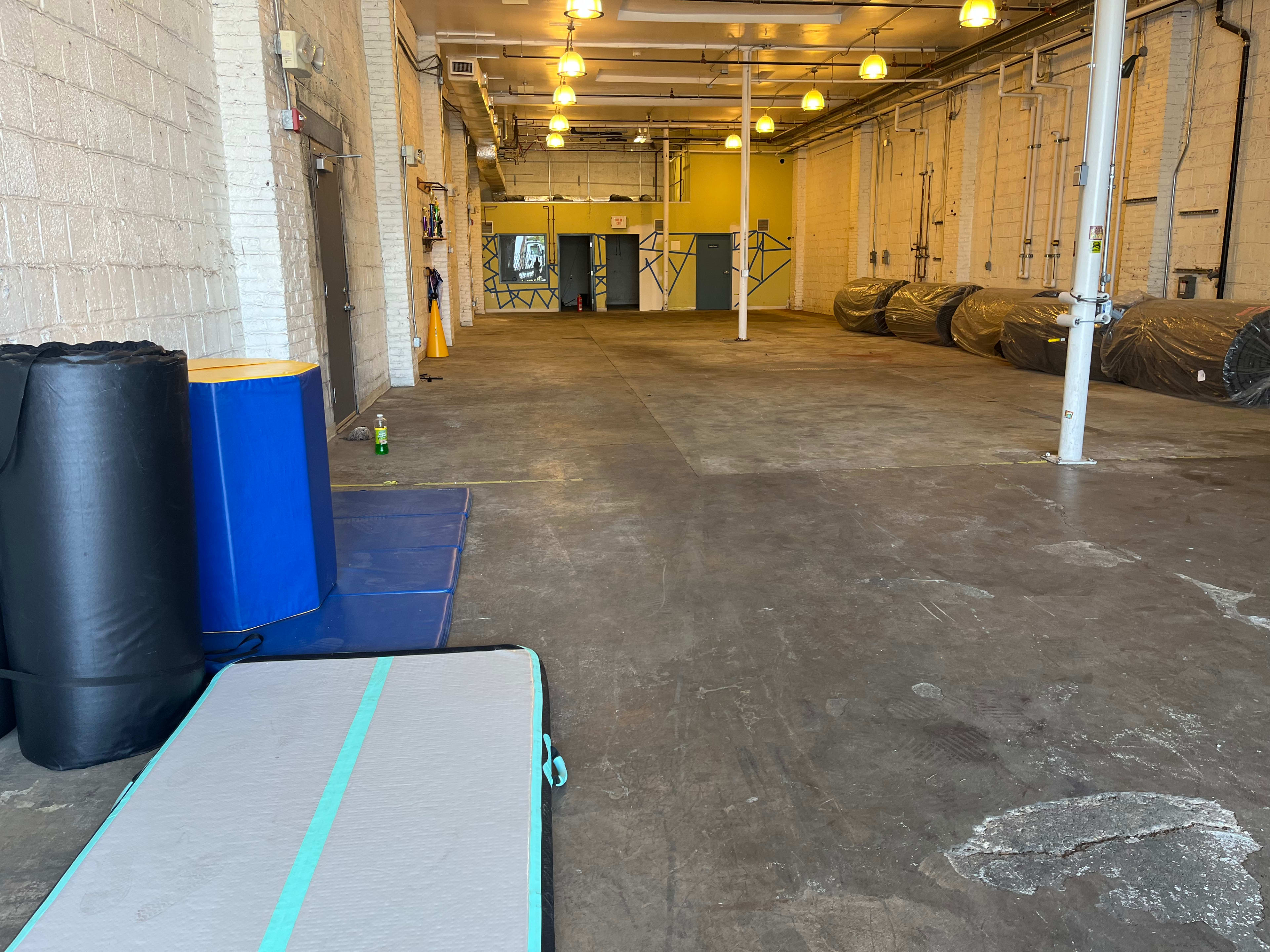 A large, empty gym space with exercise mats and equipment lined against the walls.