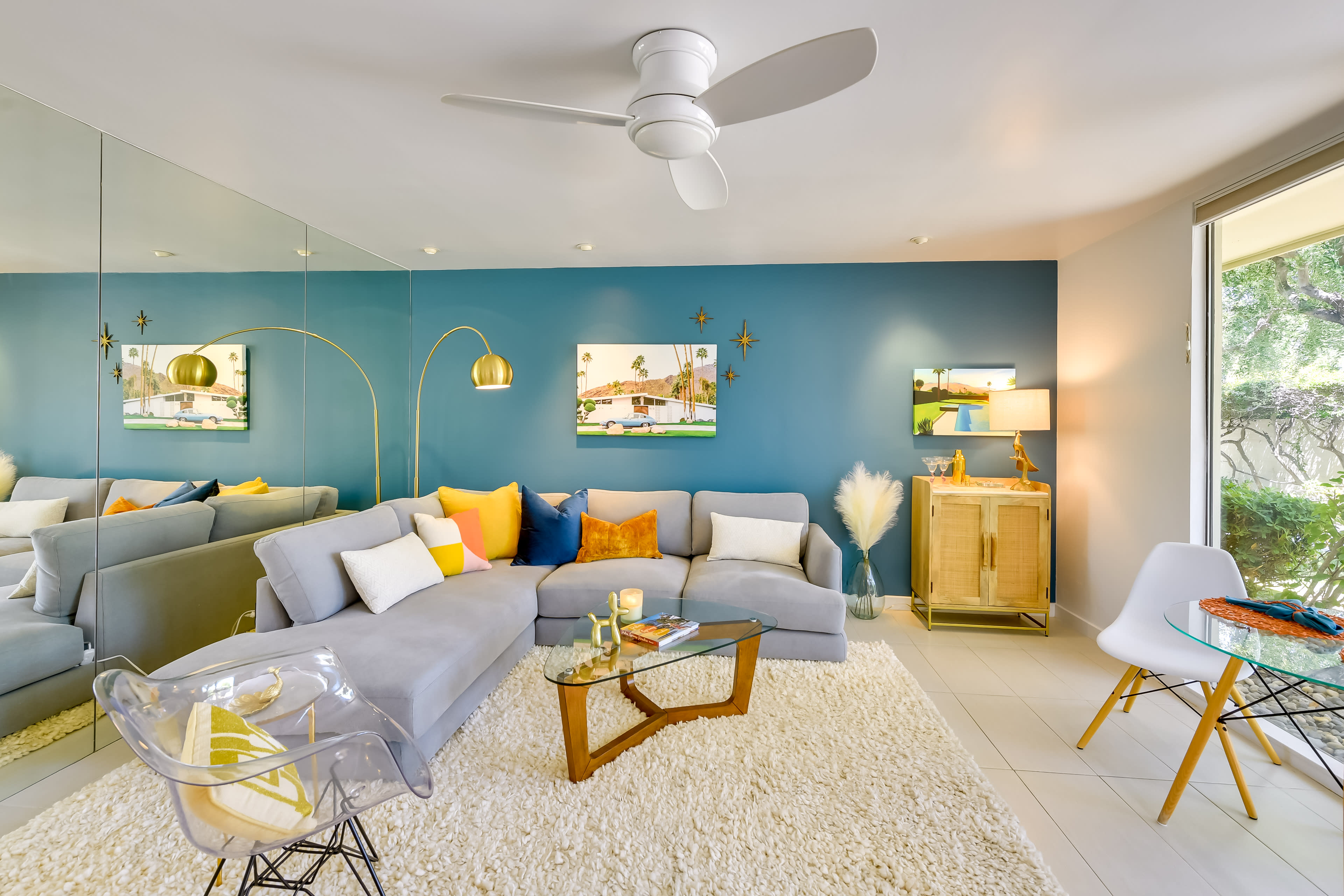 The image shows a modern living room featuring a gray sectional sofa, a wooden coffee table, and decorative wall art against a blue accent wall.