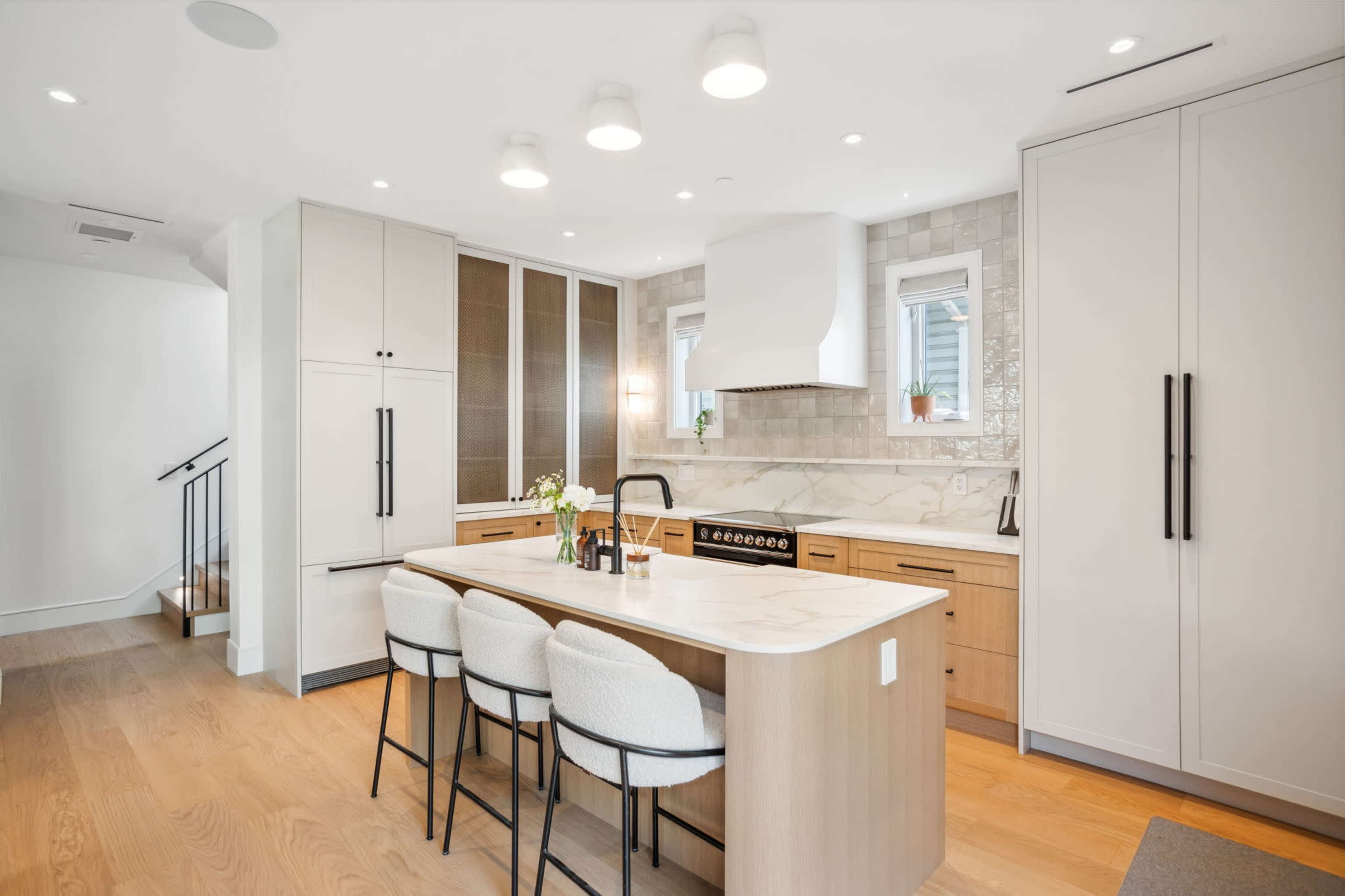 The image shows a modern kitchen featuring a large island with seating, sleek cabinetry, and stainless steel appliances.