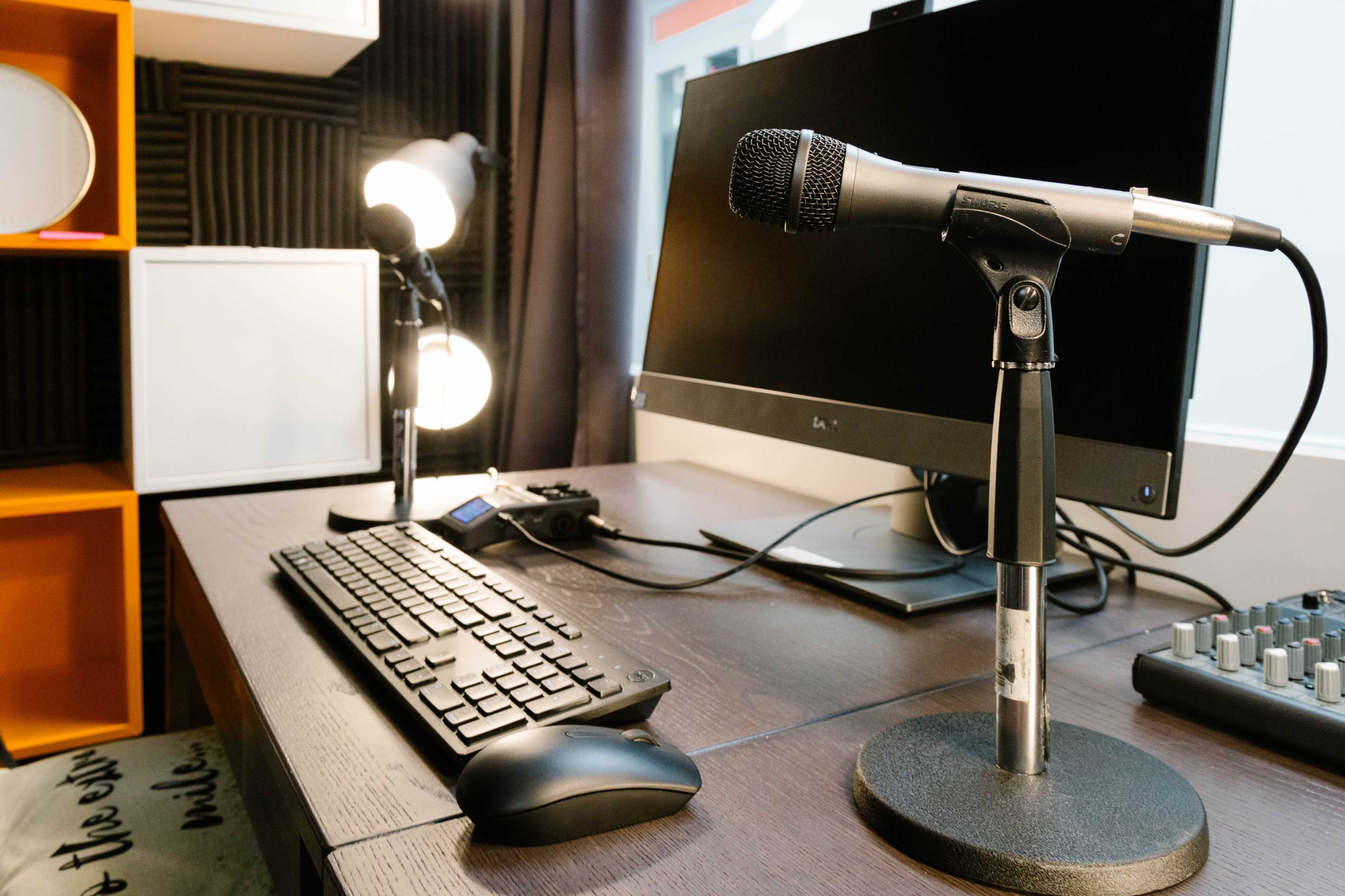 A desk setup featuring a microphone on a stand, a keyboard, a monitor, and studio lighting.