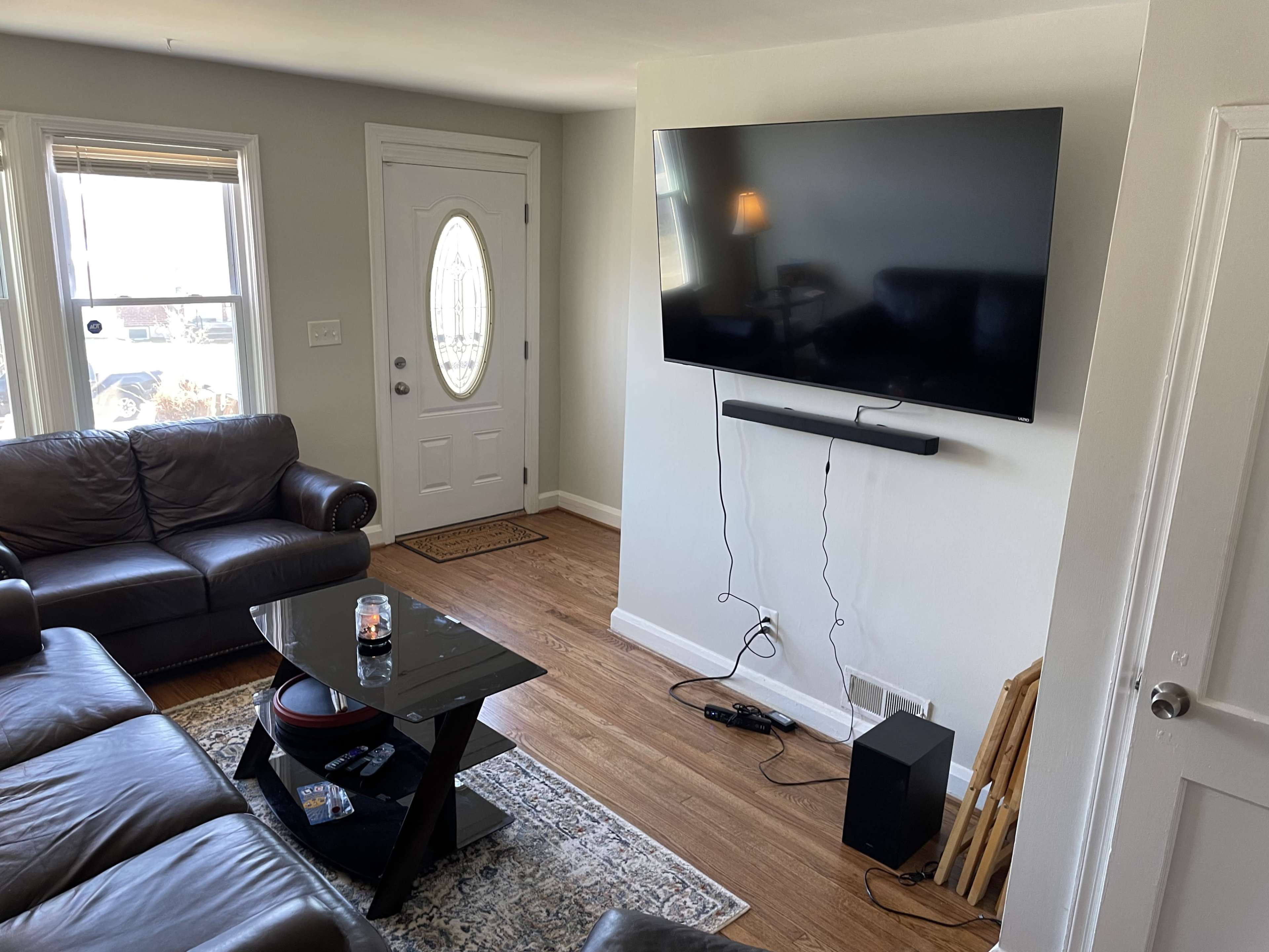 A living room with a leather sofa, a wall-mounted television, a coffee table, and a front door.