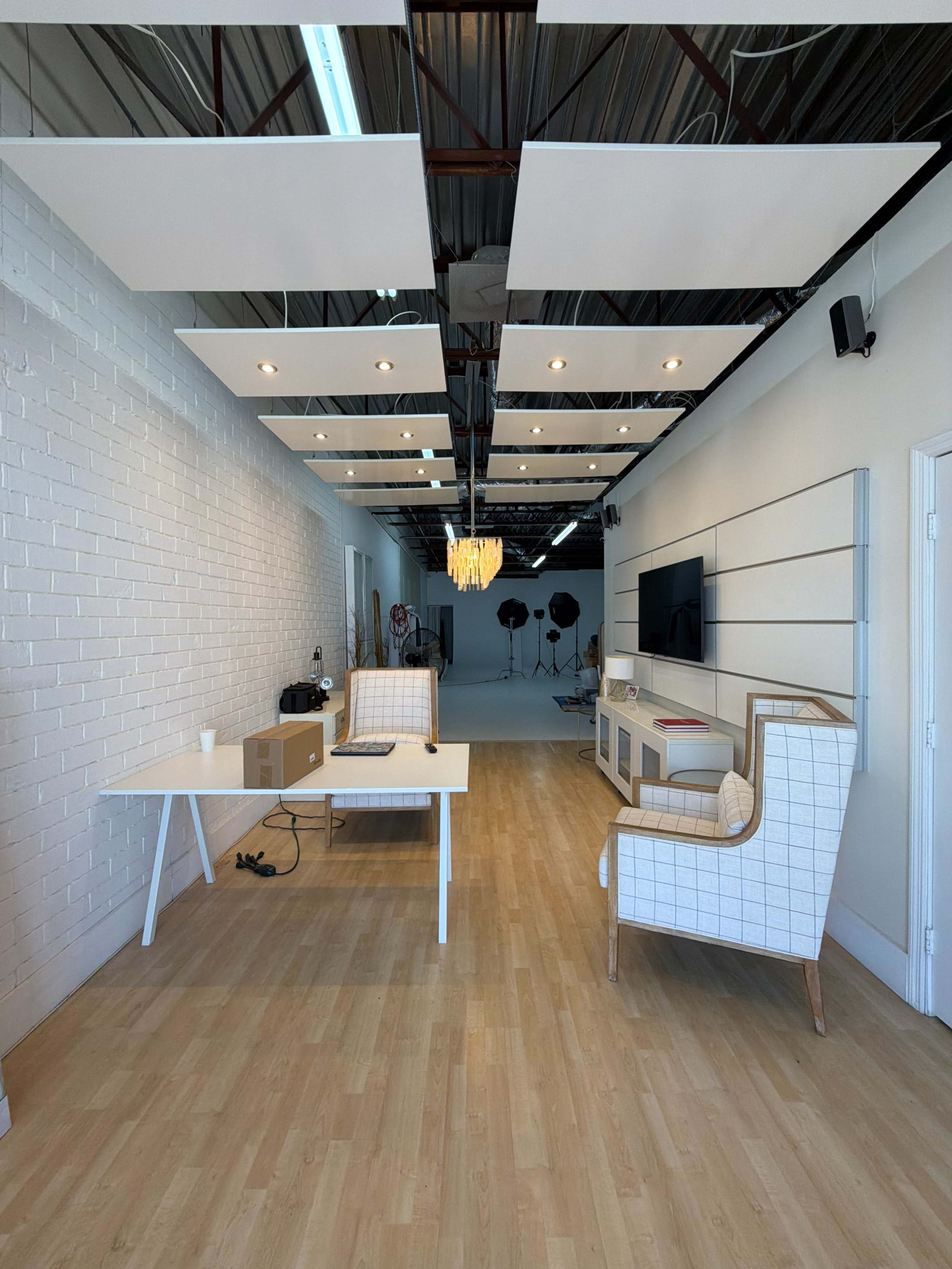 The image shows a minimalist studio space featuring a white desk, a patterned armchair, and studio lighting setups in the background.