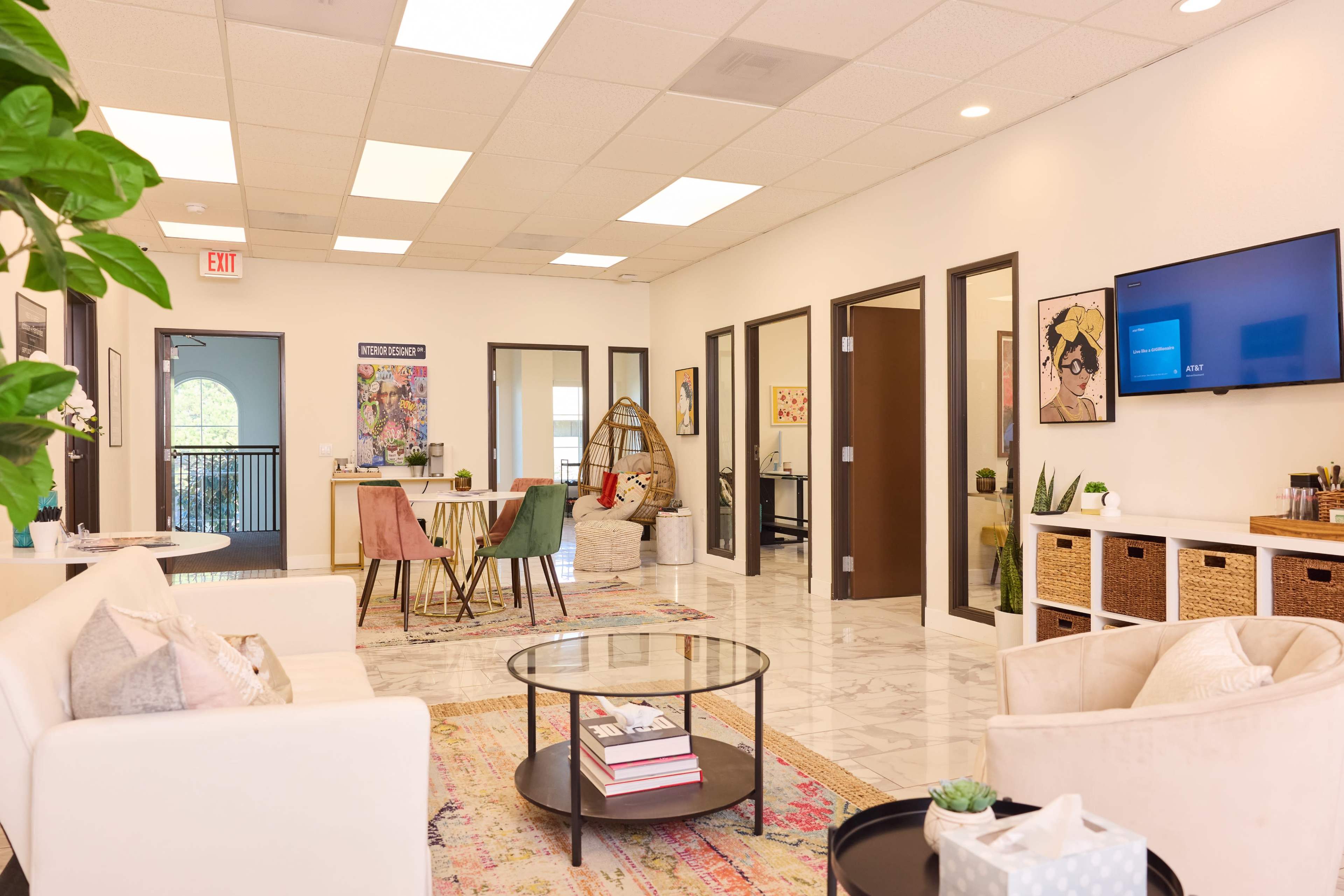 A modern office reception area featuring a seating arrangement with a coffee table, a colorful rug, and several framed artworks on the walls.