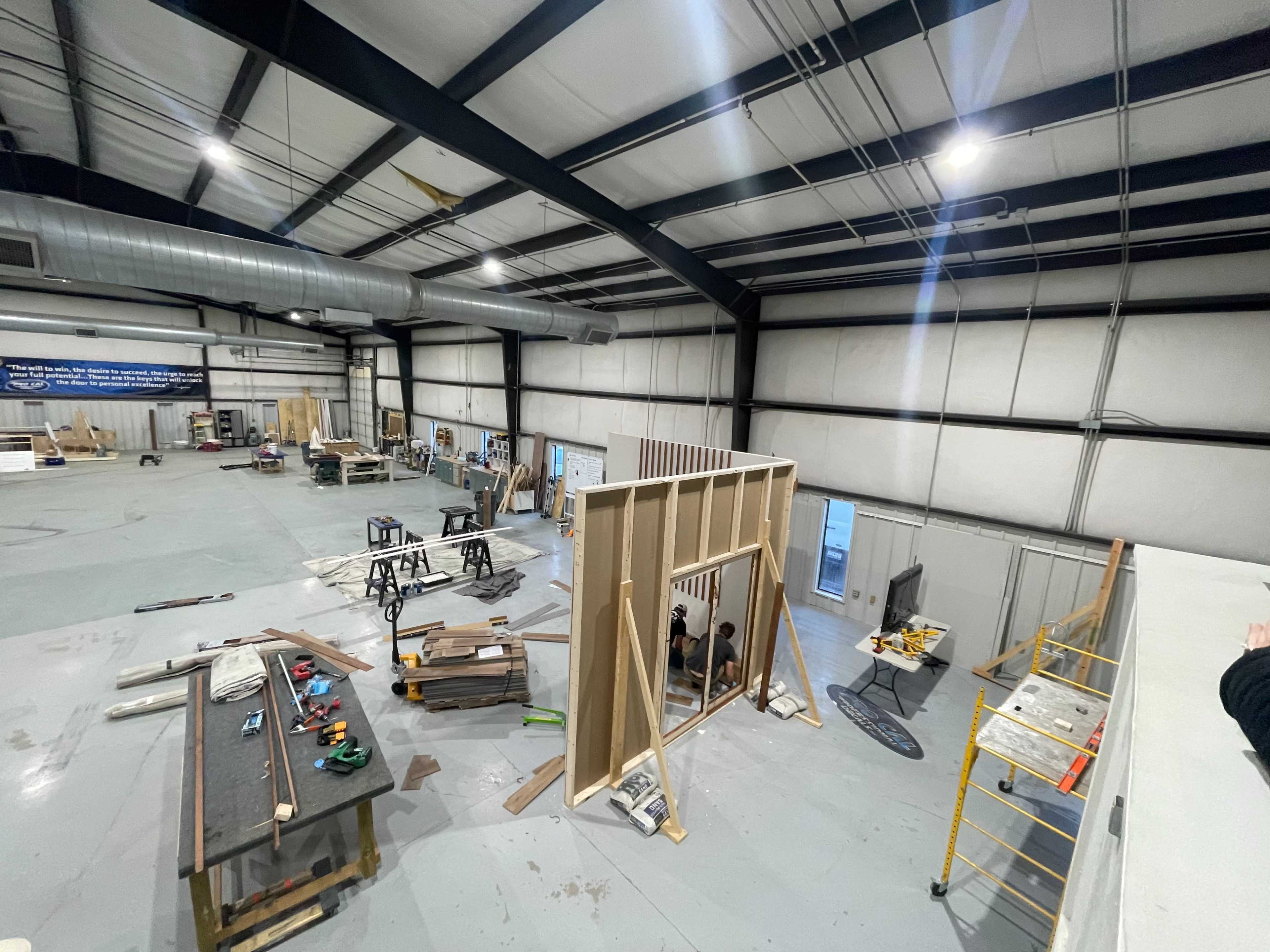 The image shows a spacious warehouse under construction, featuring various construction materials and tools scattered throughout the area.