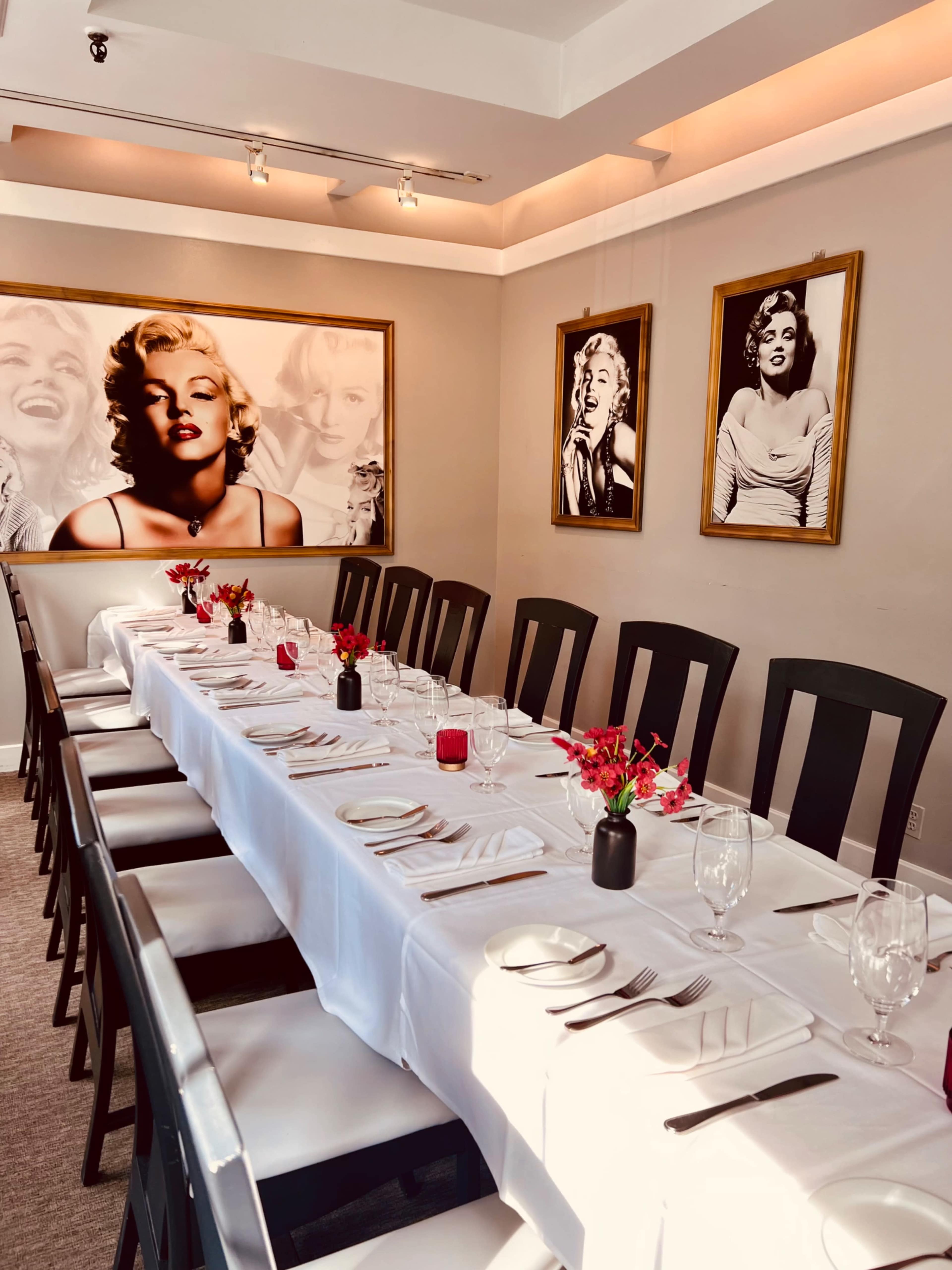 A long dining table is set for a meal in a well-decorated room featuring black and white portraits of Marilyn Monroe on the walls.