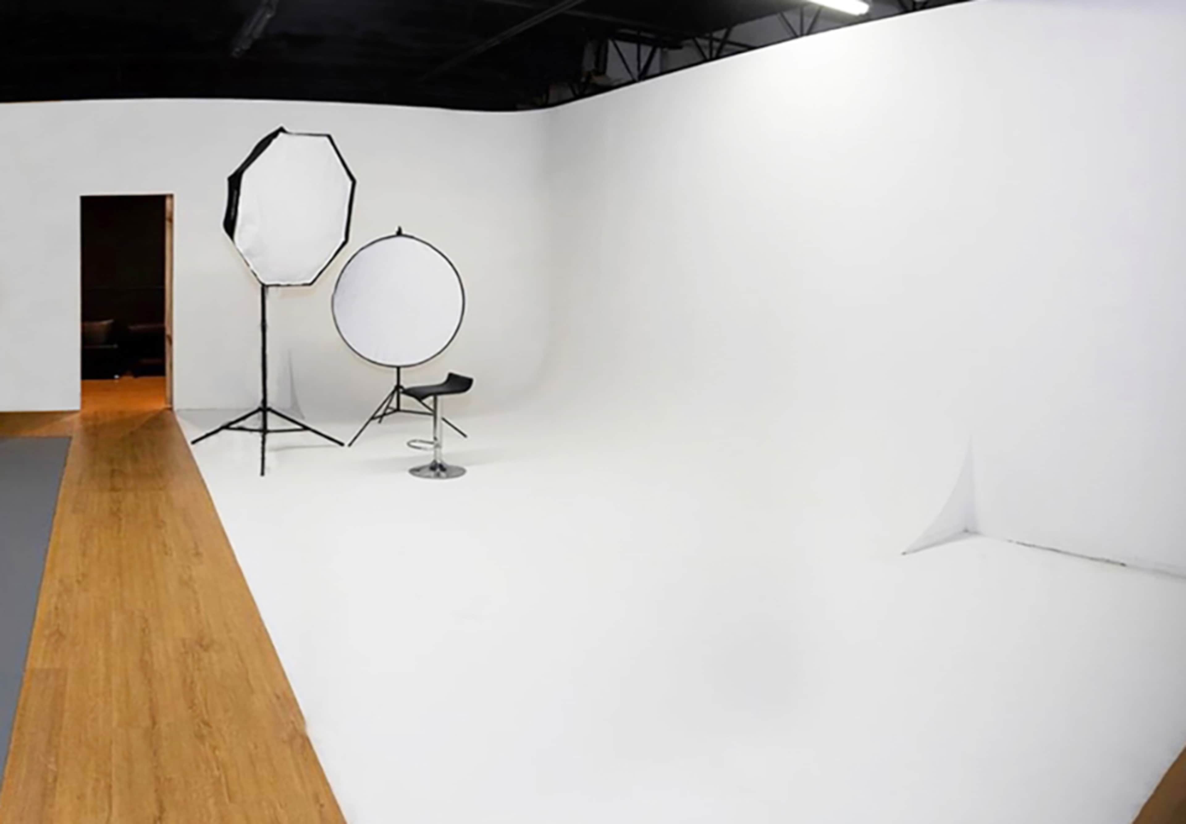 A photography studio with white walls, a smooth floor, and two light modifiers positioned near a chair.