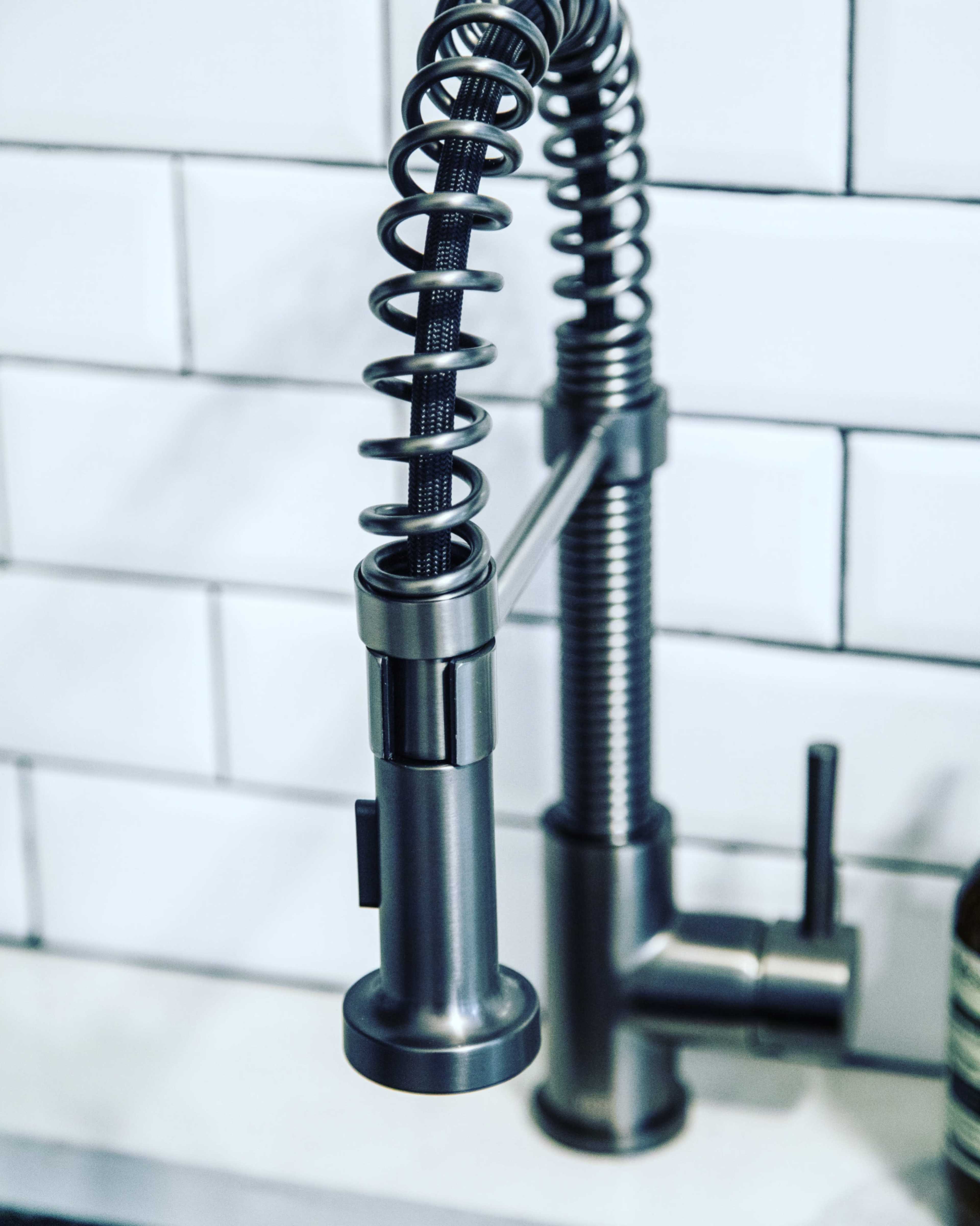 A modern kitchen faucet with a flexible, coiled neck and a sleek, metallic finish against a backdrop of white subway tiles.
