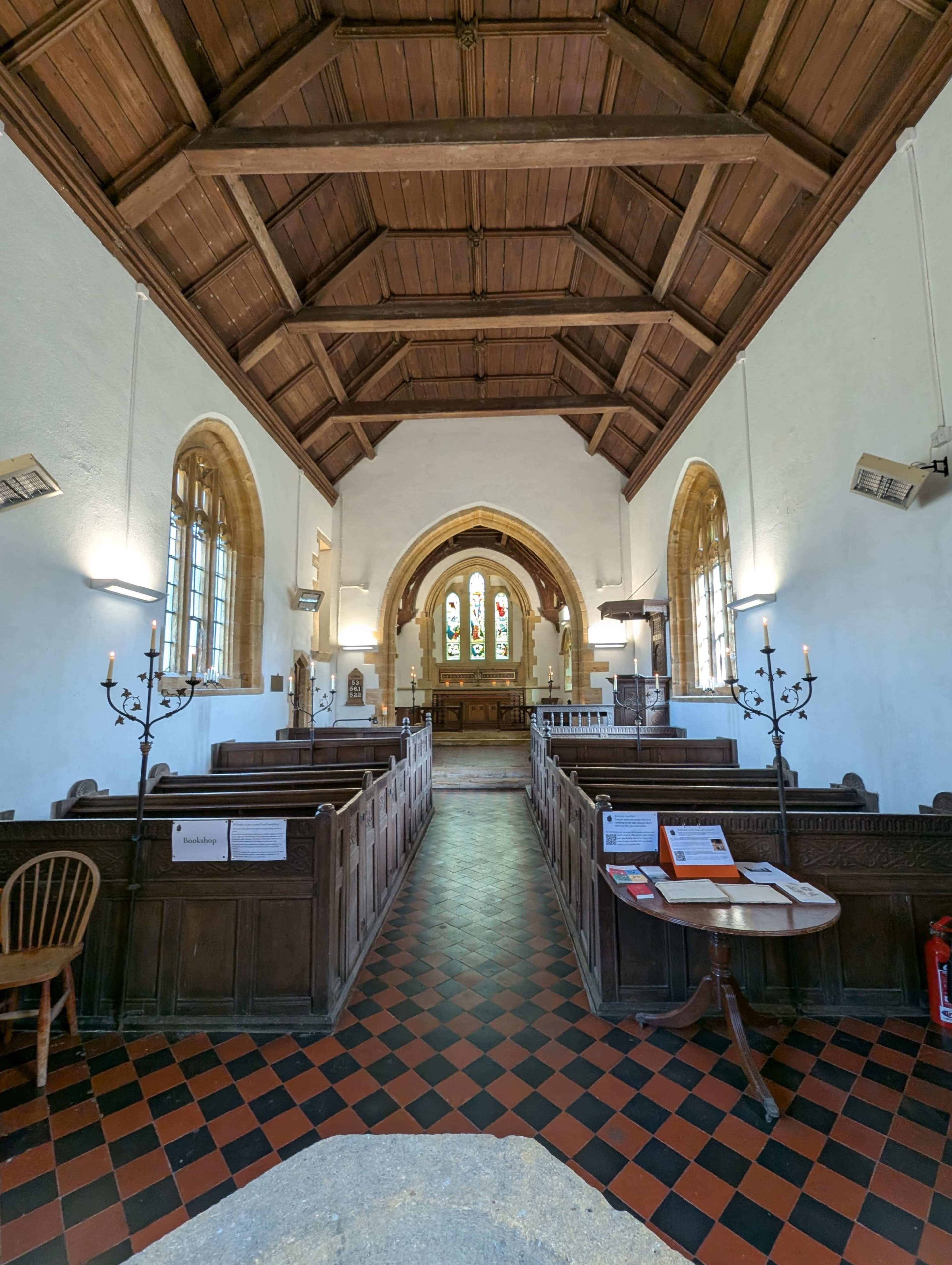 The interior of a church features wooden pews, a high wooden ceiling, and stained glass windows at the front.