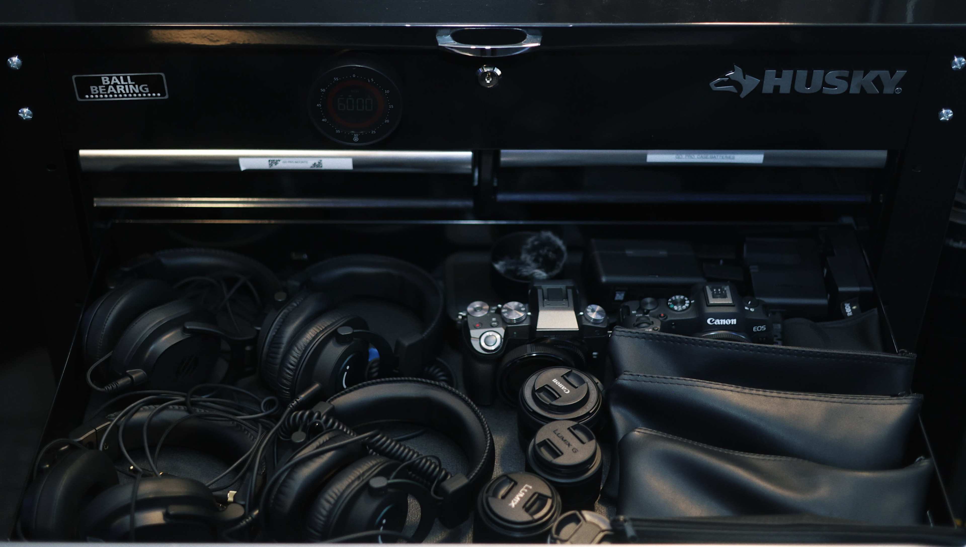 A black storage drawer contains various photography equipment, including cameras, lenses, headphones, and a digital display.