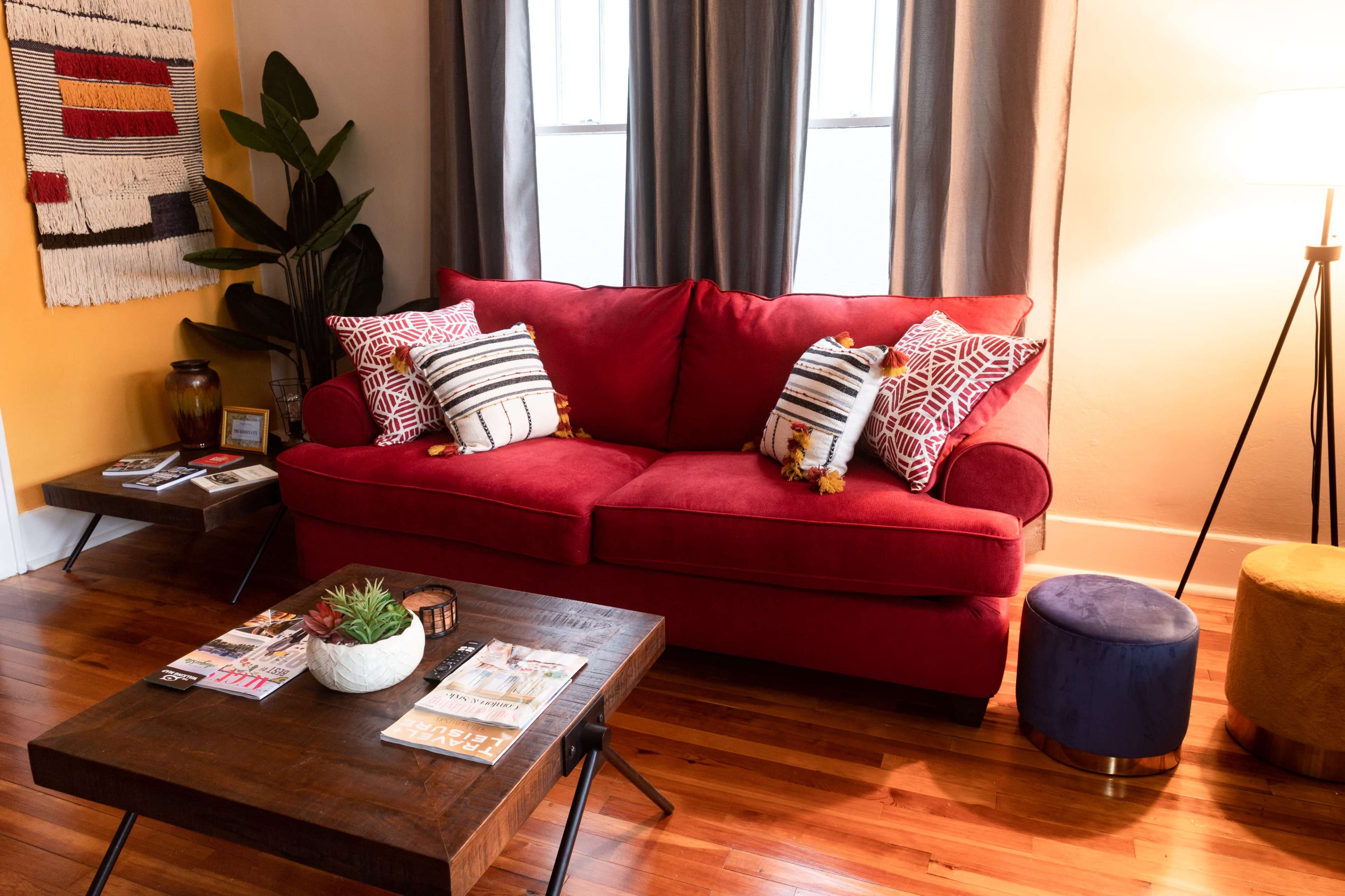 A red sofa is positioned next to a wooden coffee table, with decorative pillows, a plant, and a lamp illuminating the space.
