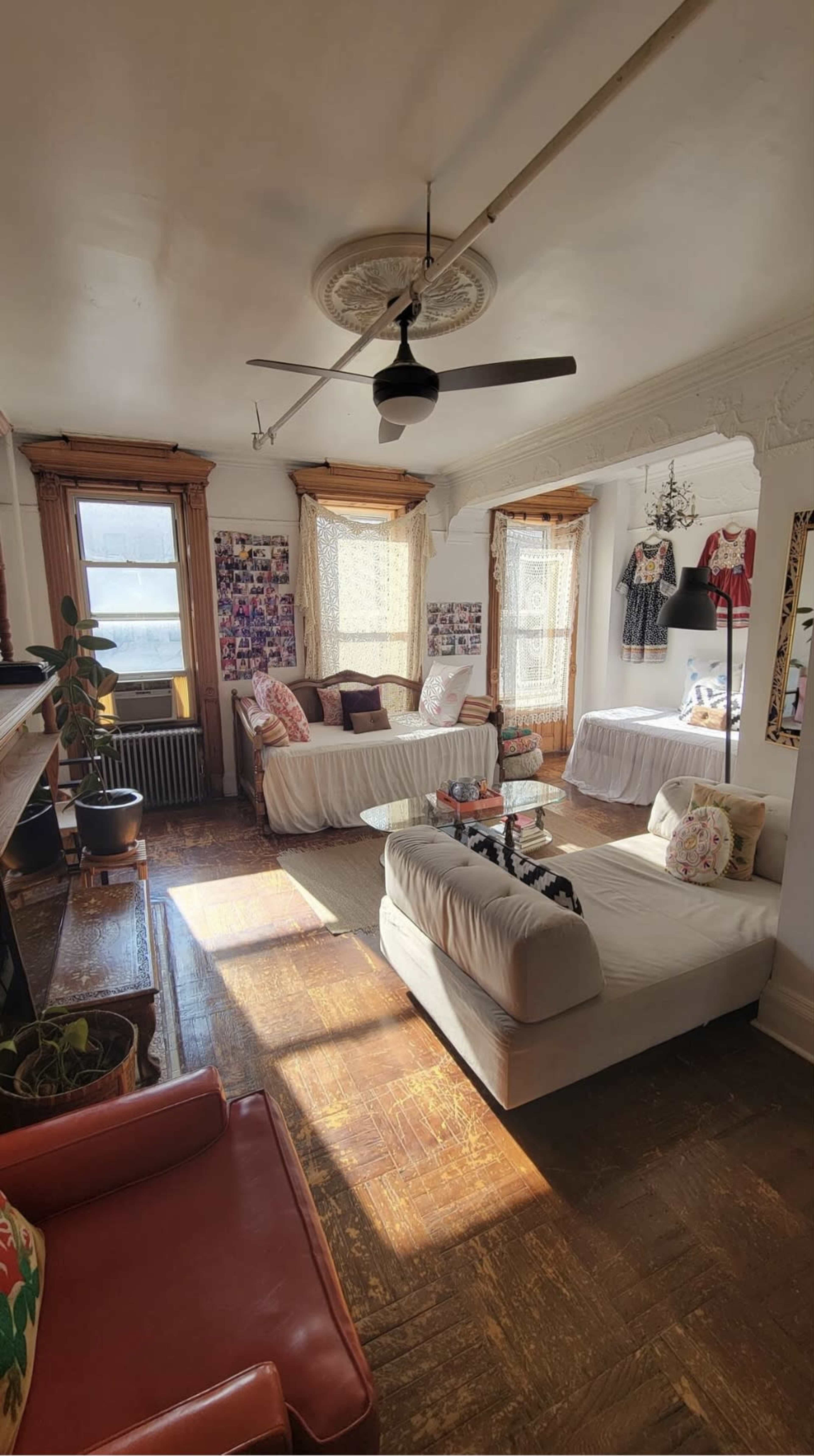 The image shows a bright living room with two white sofas arranged around a coffee table, large windows with curtains, and decorative wall elements.