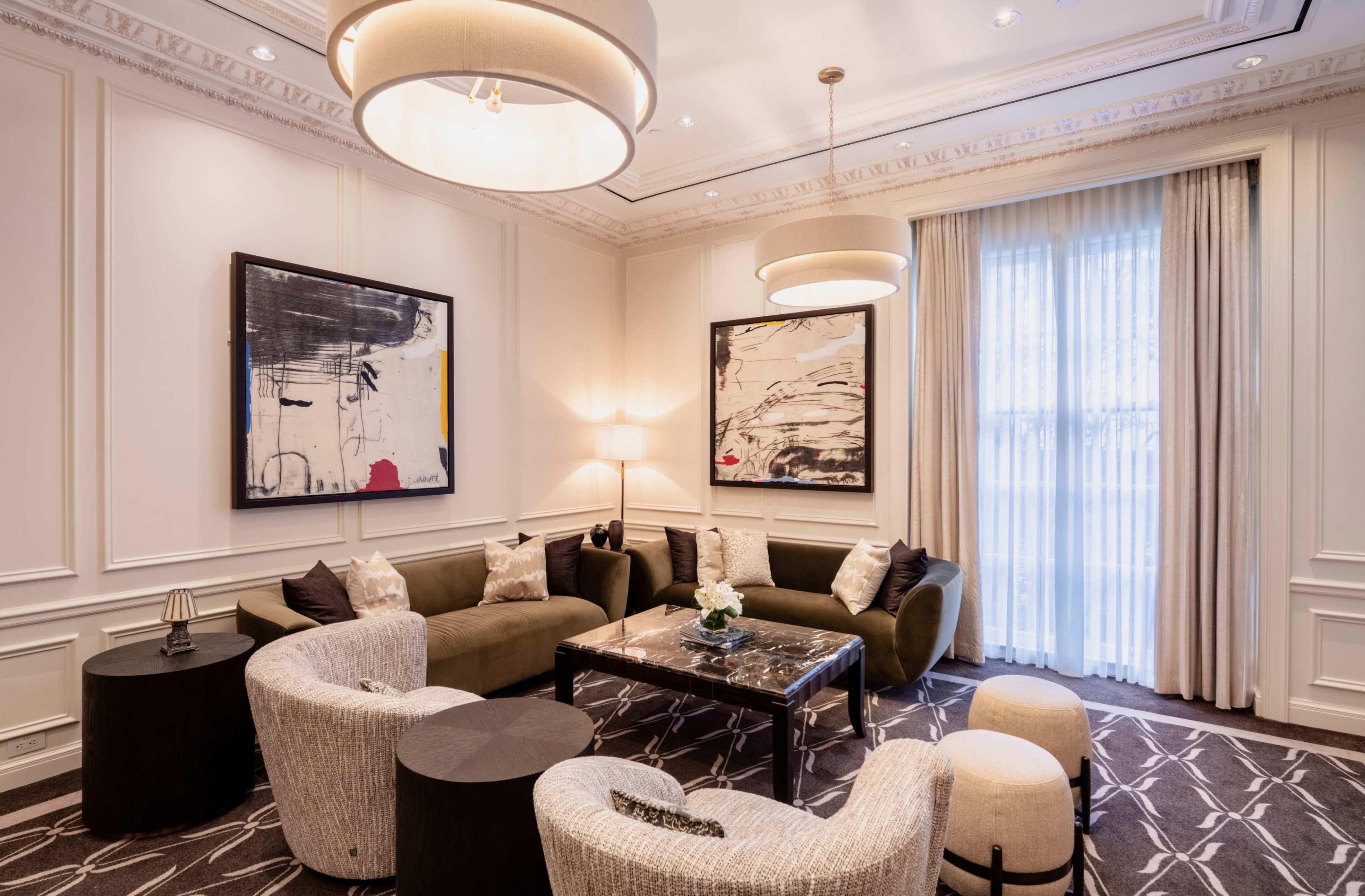 The image shows a stylish lounge area featuring a modern seating arrangement with two sofas, several accent chairs, a coffee table, and artworks on the walls.