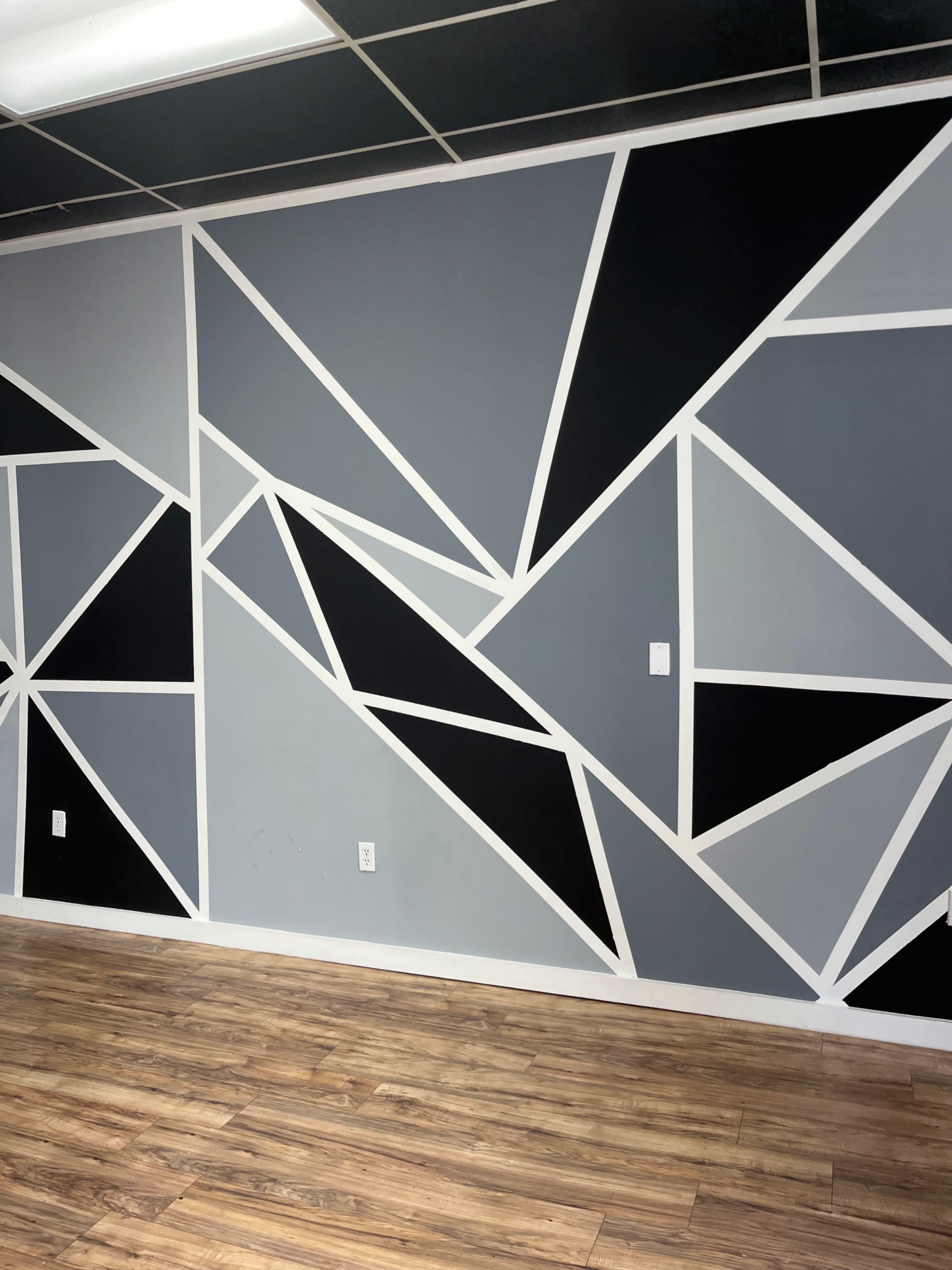 A wall with a geometric mural featuring triangles in varying shades of gray and black, outlined with white.
