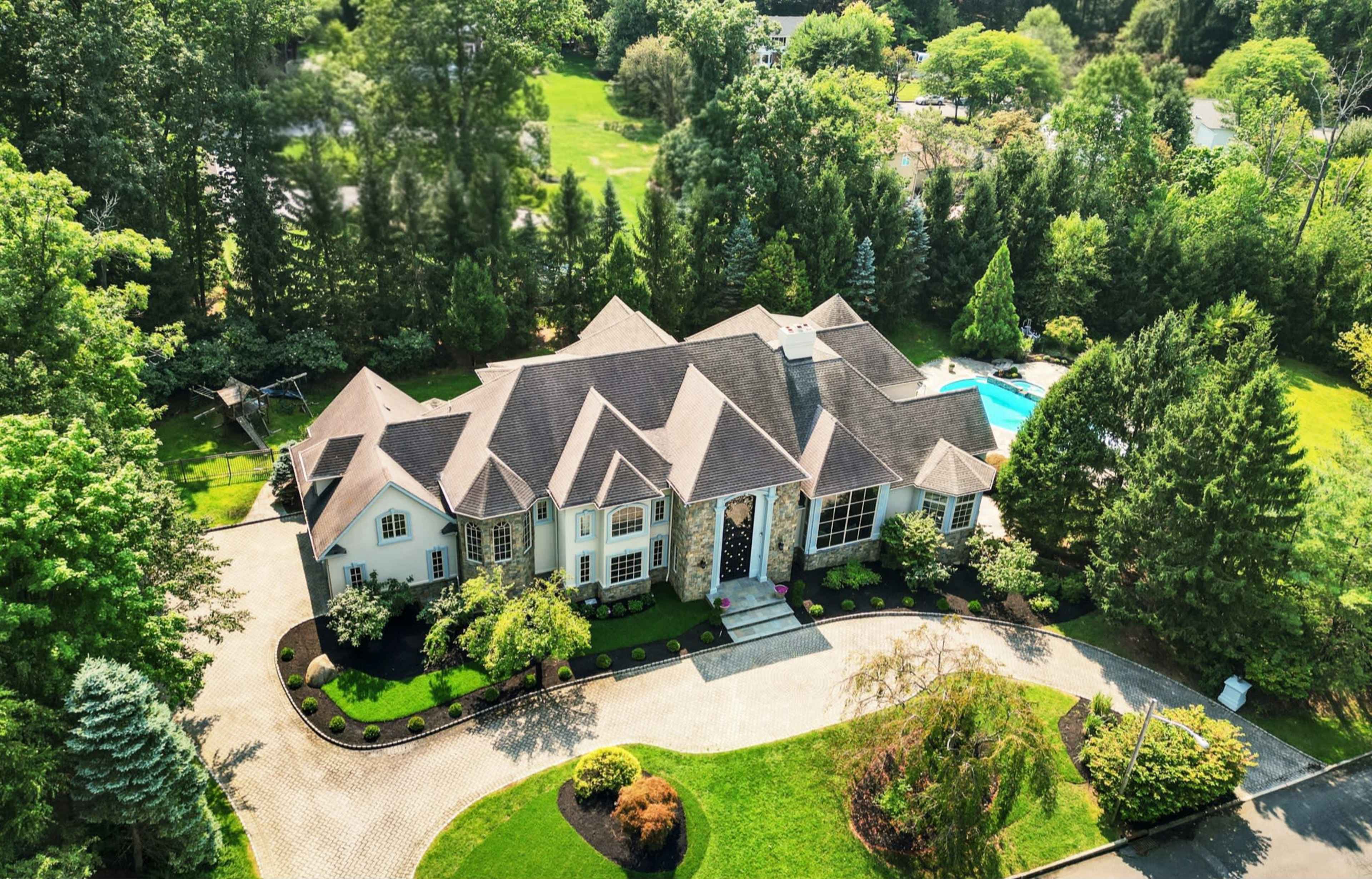 The image shows a spacious, modern house with a well-maintained garden and a swimming pool surrounded by trees.