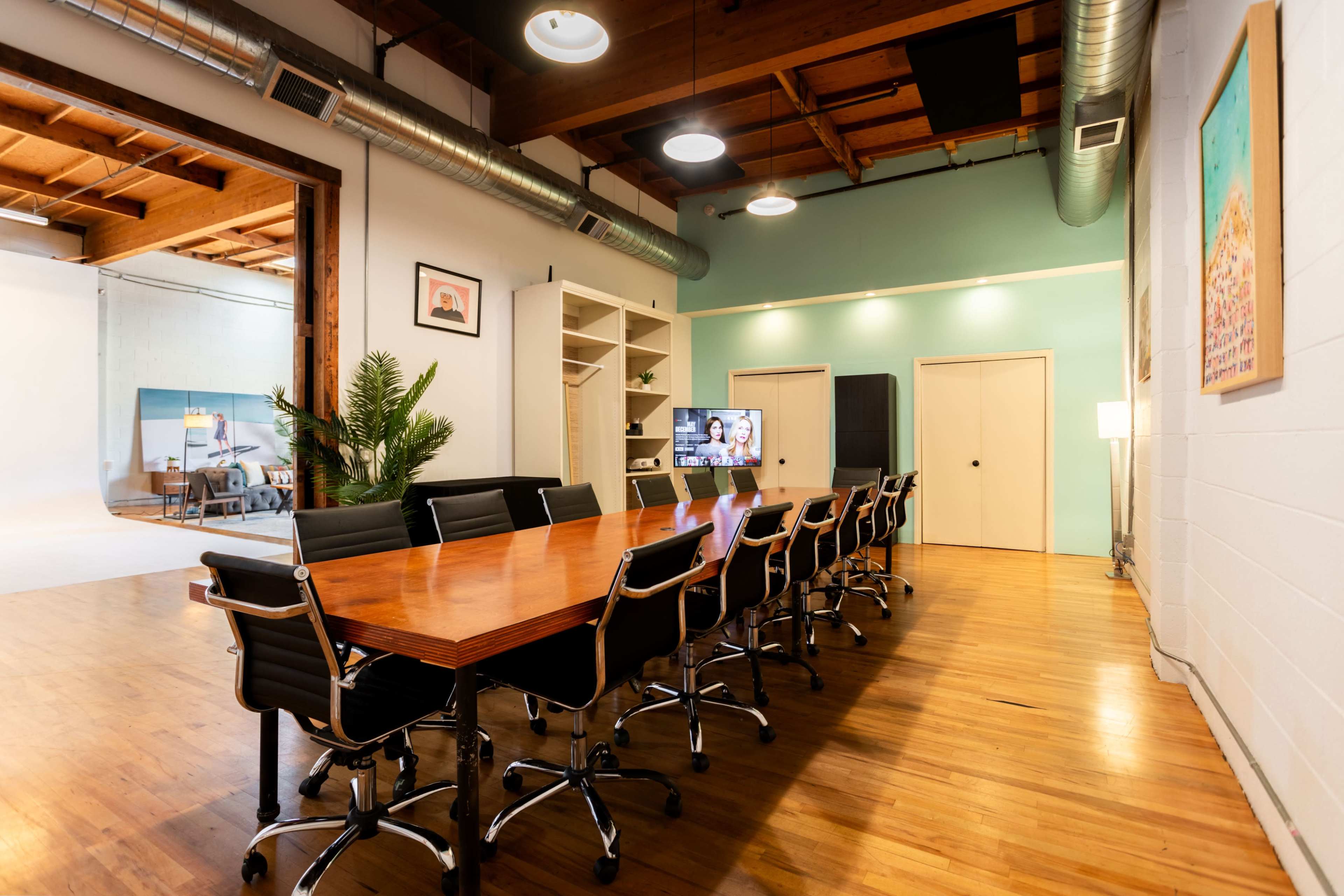 A large conference room features a long wooden table surrounded by black chairs, with a green wall and modern decor in the background.