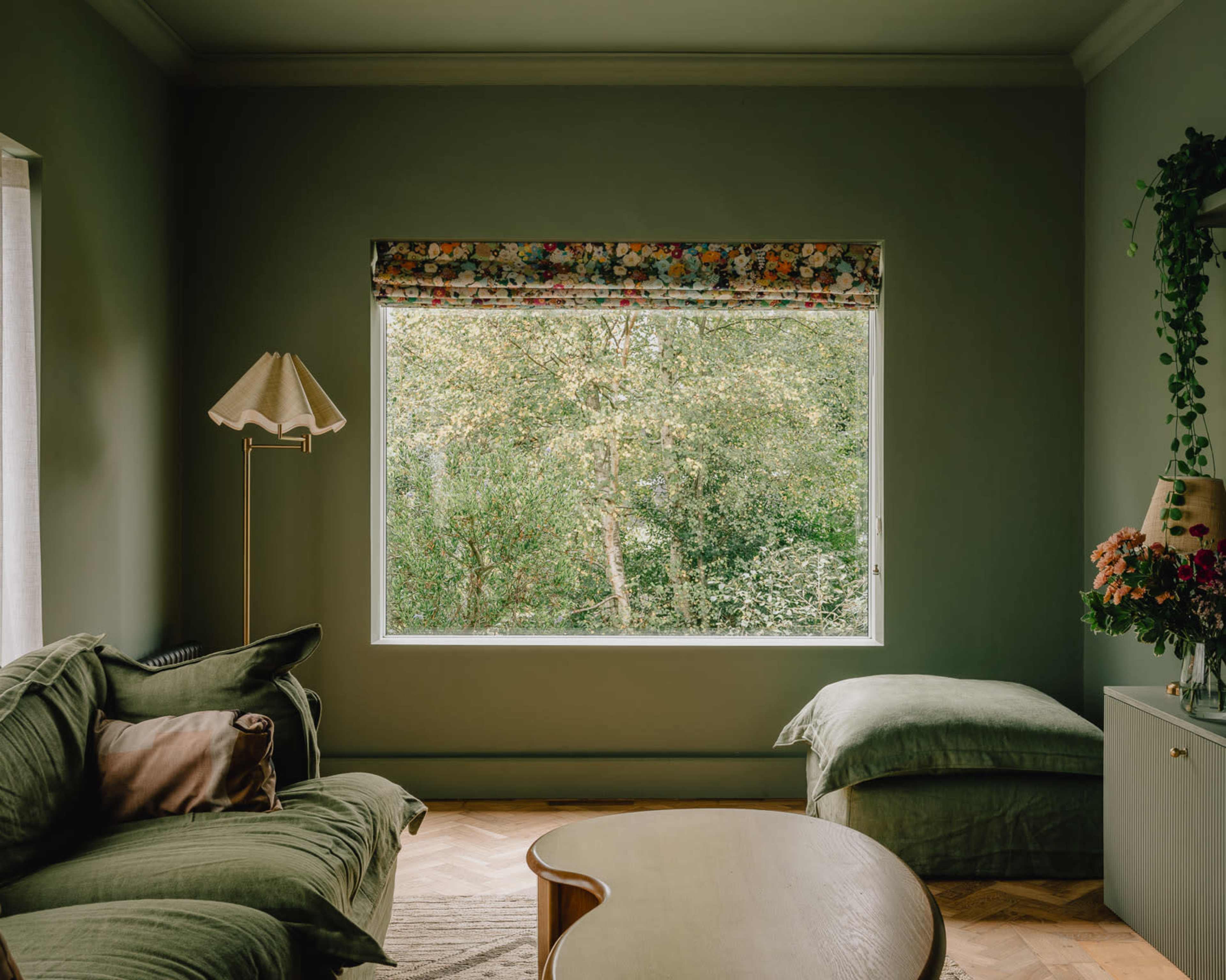The image shows a cozy living room with a green sofa, a side lamp, and a large window revealing greenery outside.