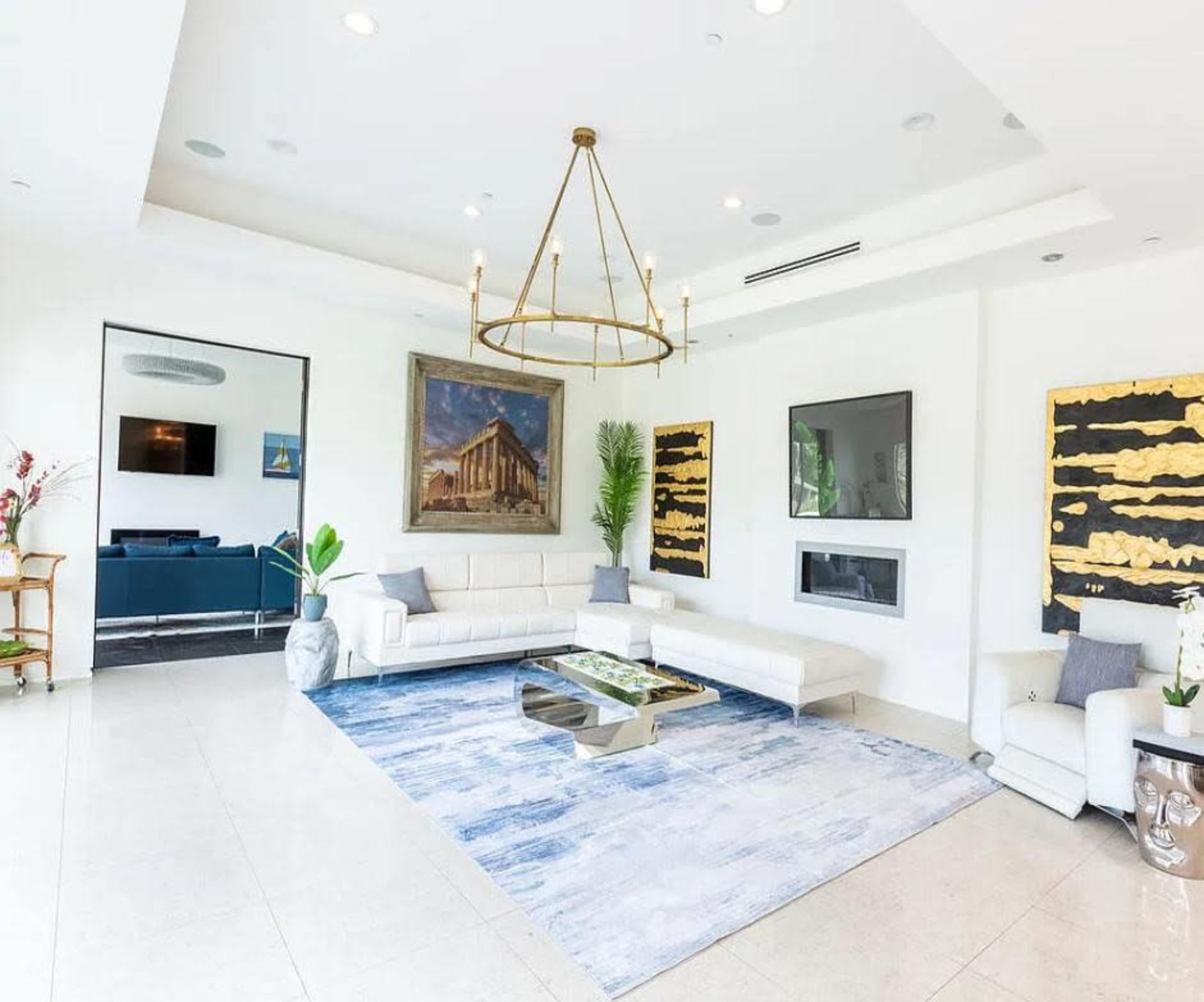 The image shows a modern living room featuring a white sectional sofa, a large area rug, contemporary artwork on the walls, and a sleek fireplace.