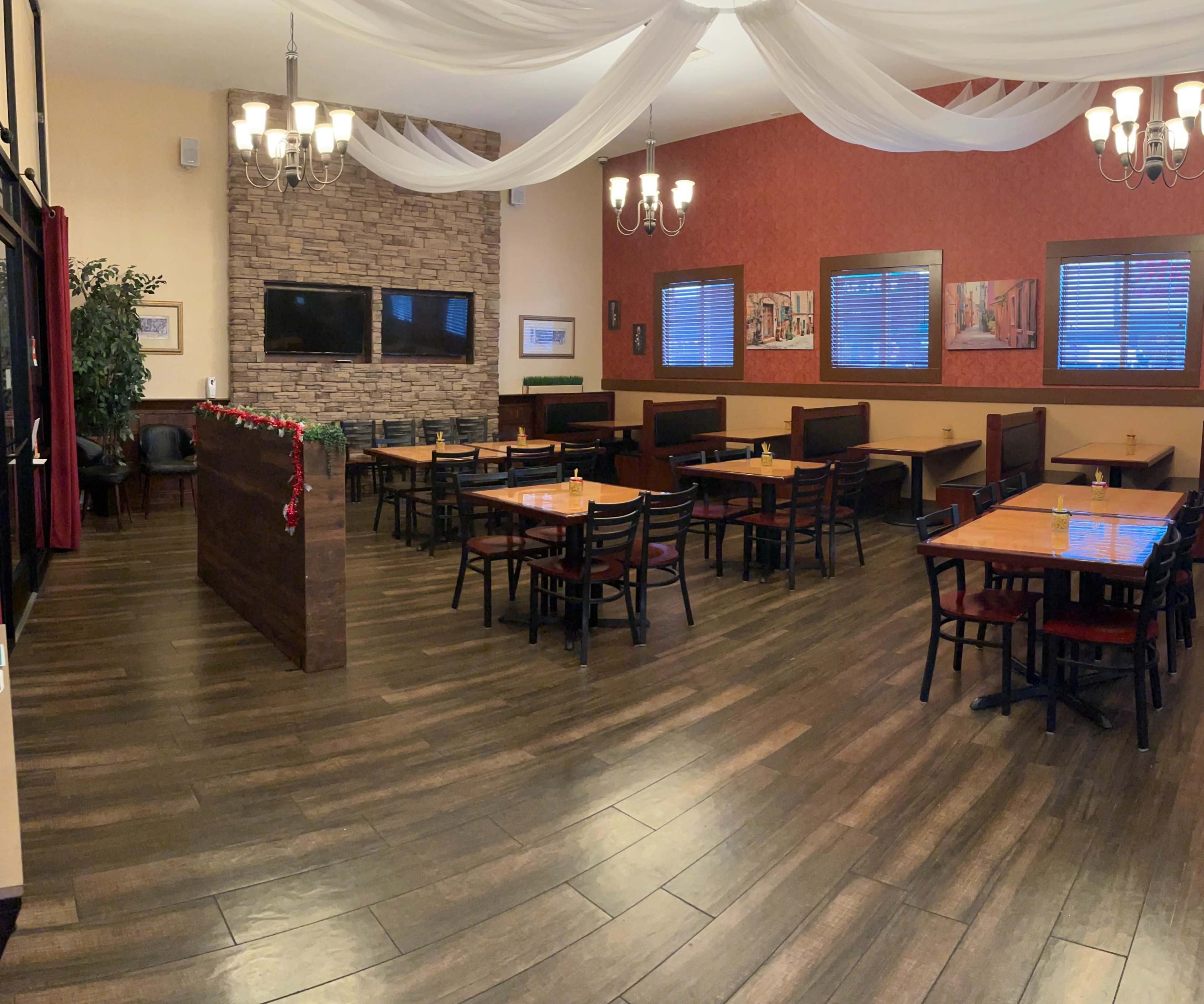 A restaurant interior with wooden tables and chairs arranged around a partially separated dining area, featuring stone and fabric decor.