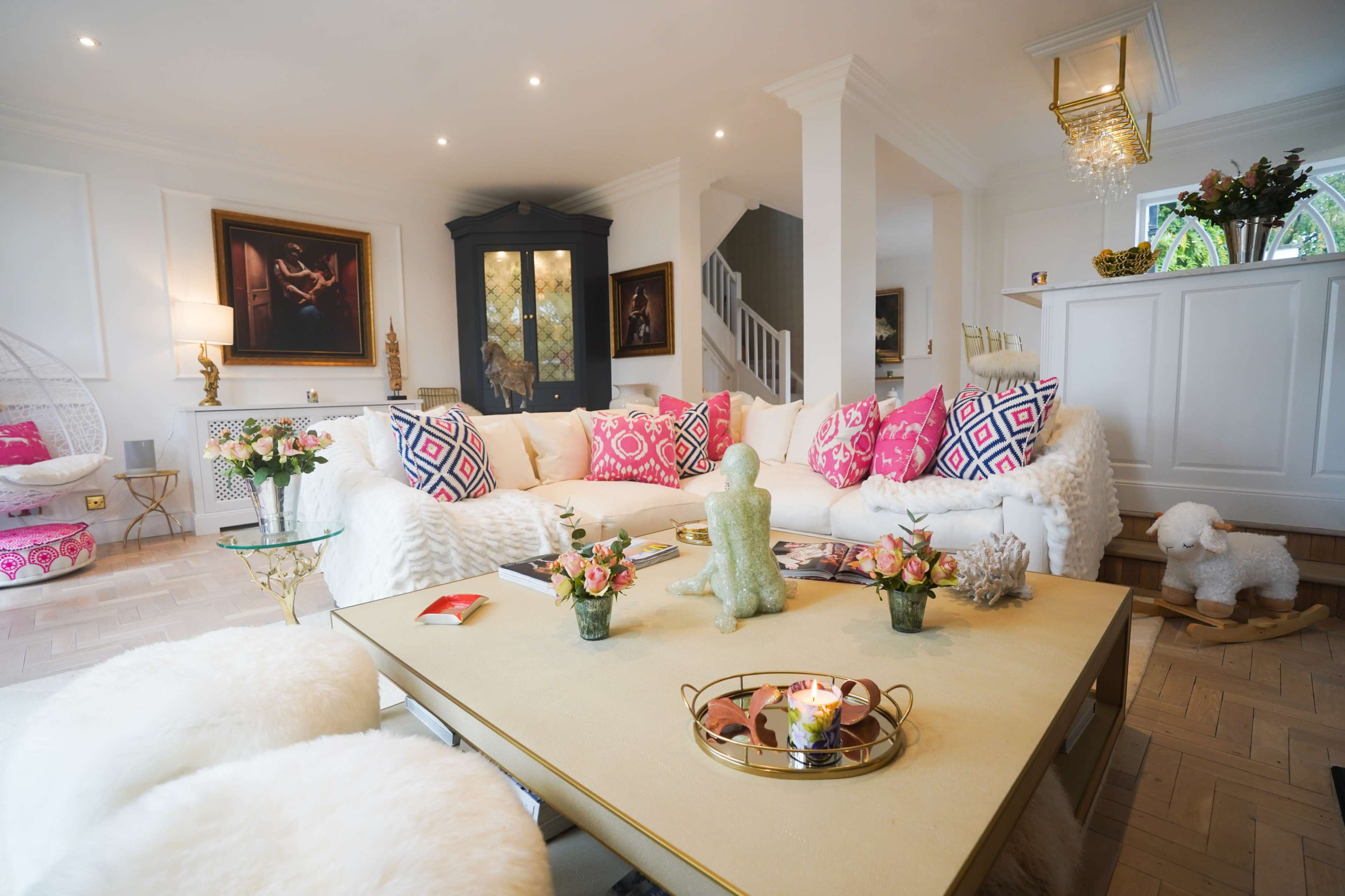 A modern living room with a plush white sofa, decorative pillows, a coffee table with flowers and a candle, and art pieces on the walls.