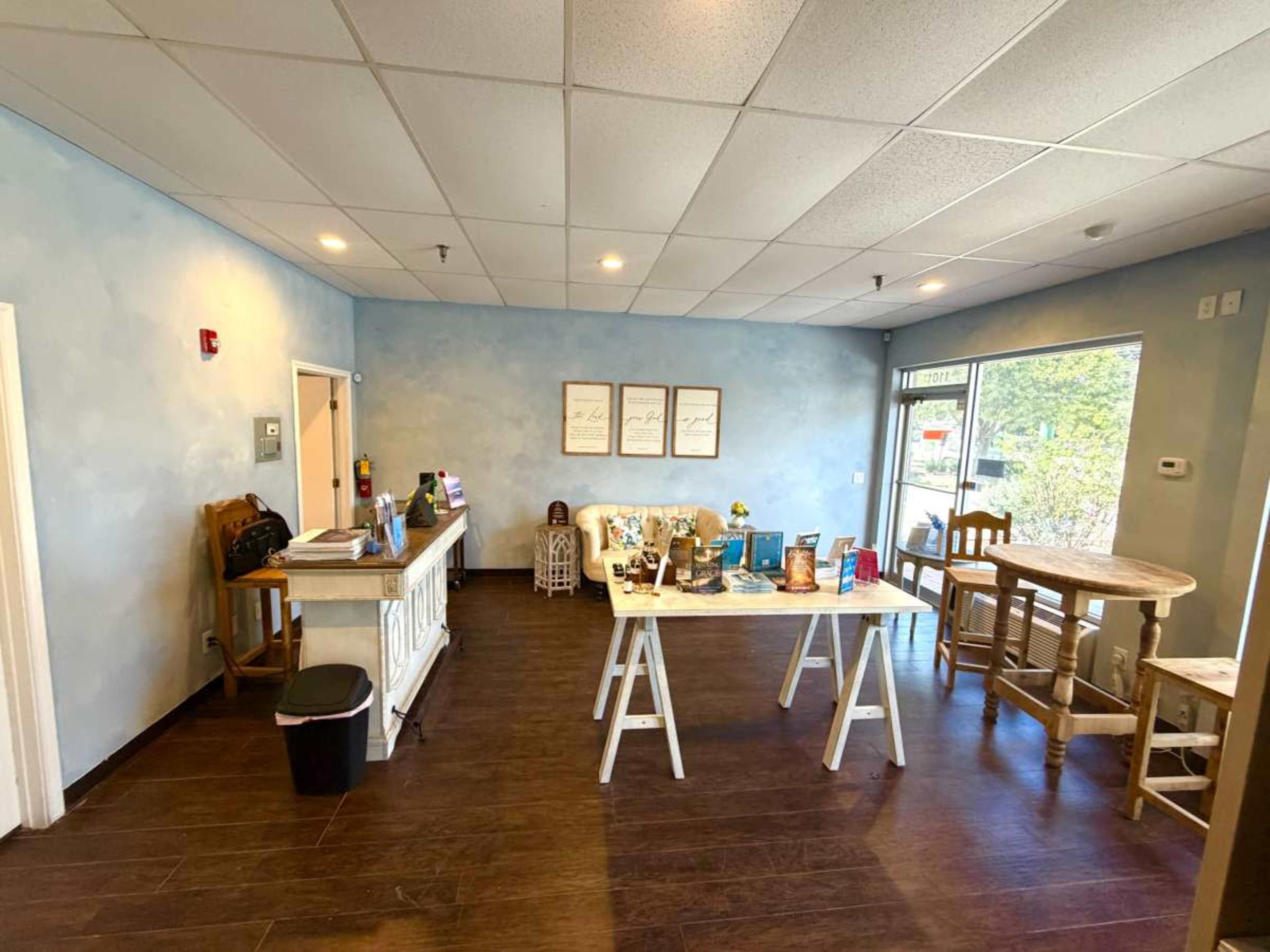 The image shows a small, tidy cafe interior with a reception area featuring a counter and several tables arranged for customers.