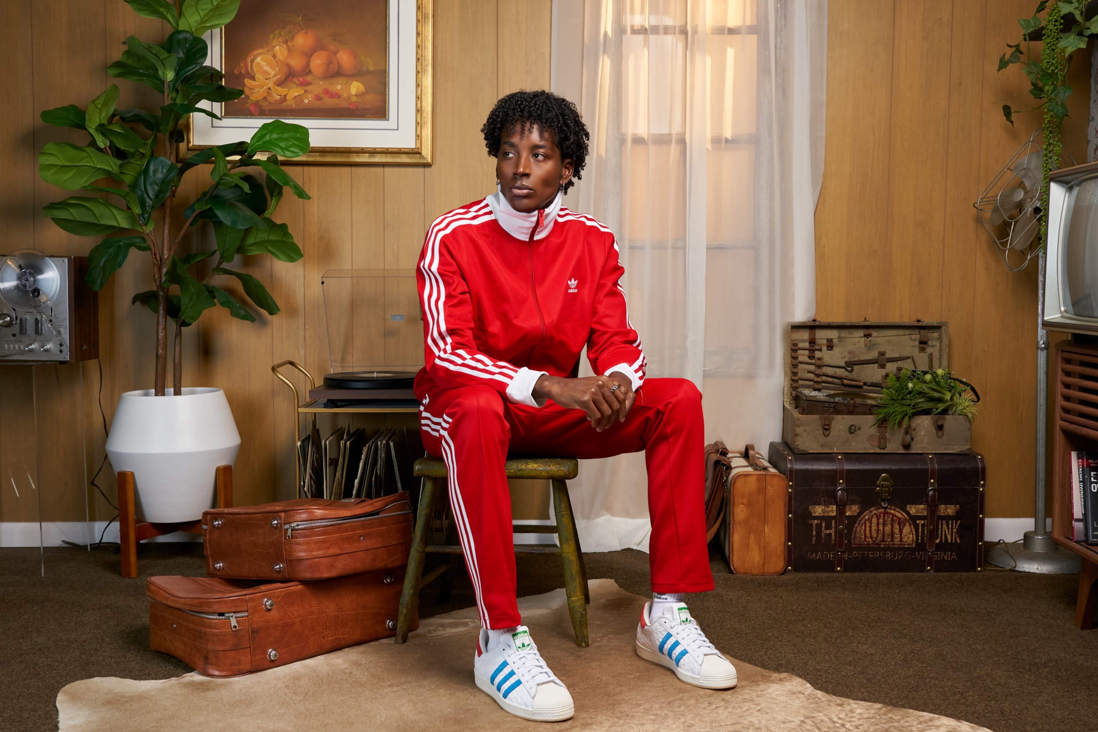 A person in a red tracksuit sits on a wooden chair in a room with wood-paneled walls and various vintage decor items.