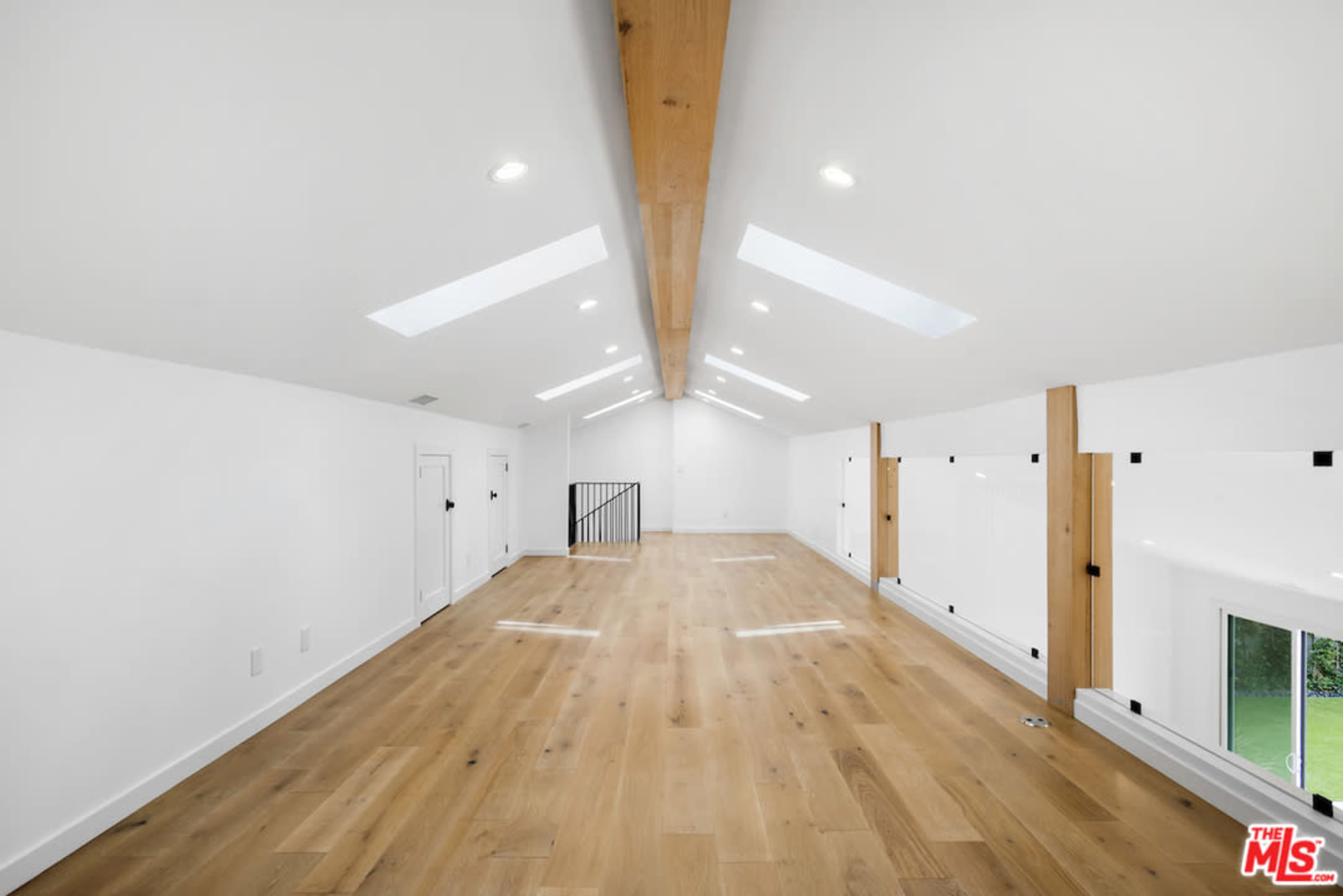 A spacious, light-filled room with wooden flooring and sloped ceilings featuring skylights and wooden beams.