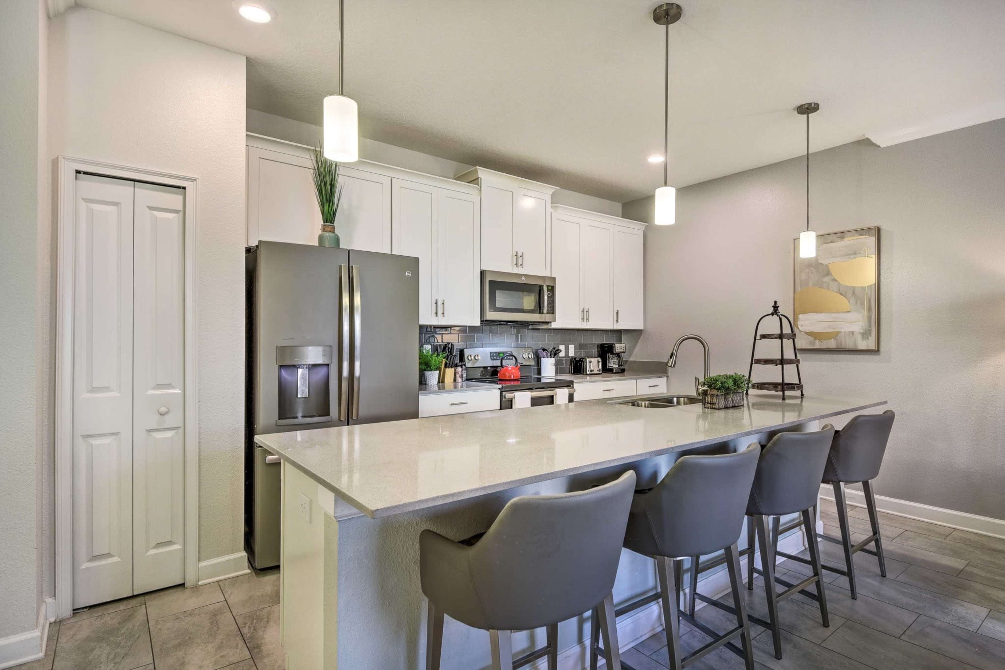 The image shows a modern kitchen with white cabinets, a large island with seating for four, and stainless steel appliances.