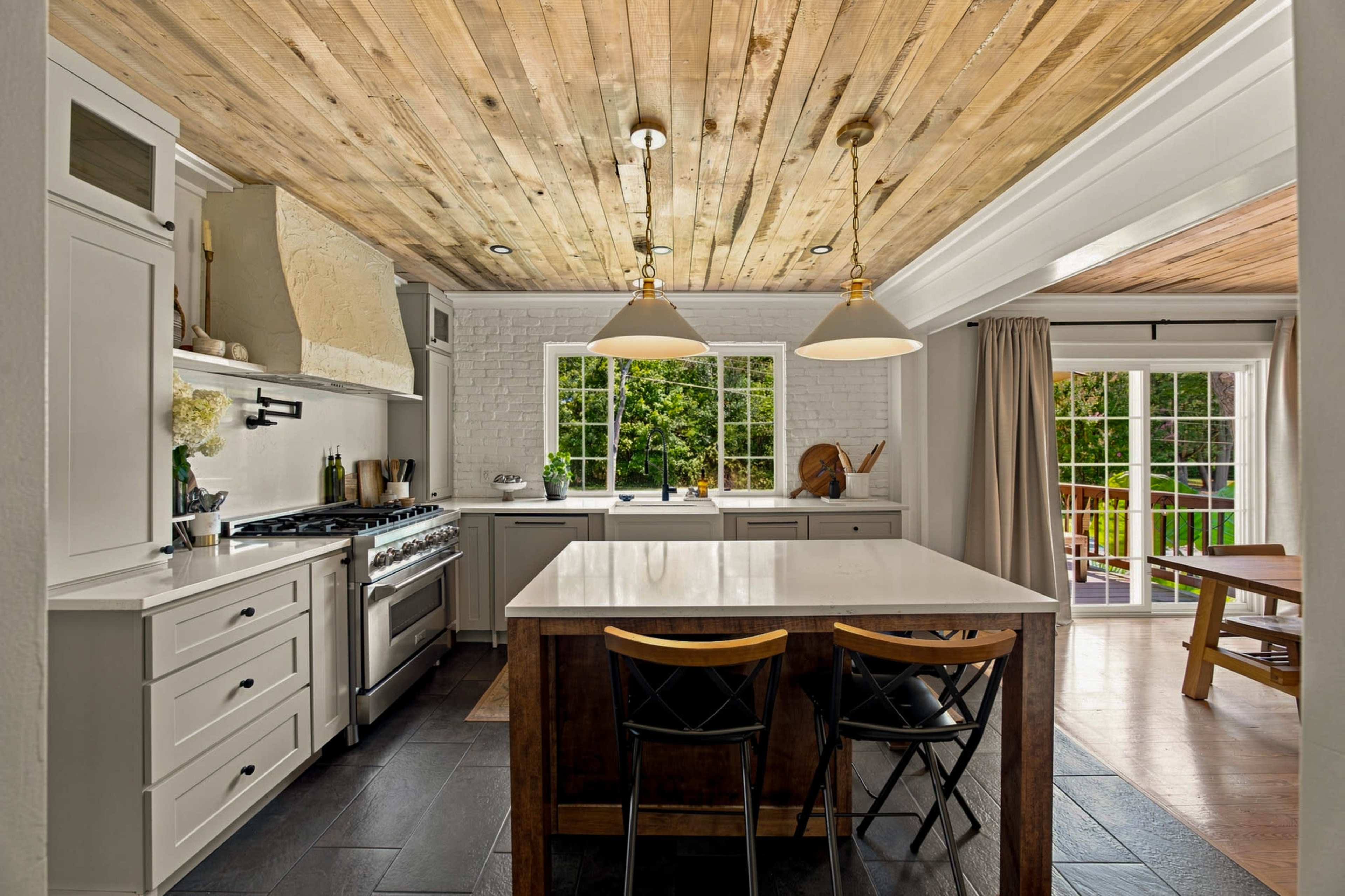 The kitchen features a central island with bar seating, white cabinetry, and a wooden ceiling above.