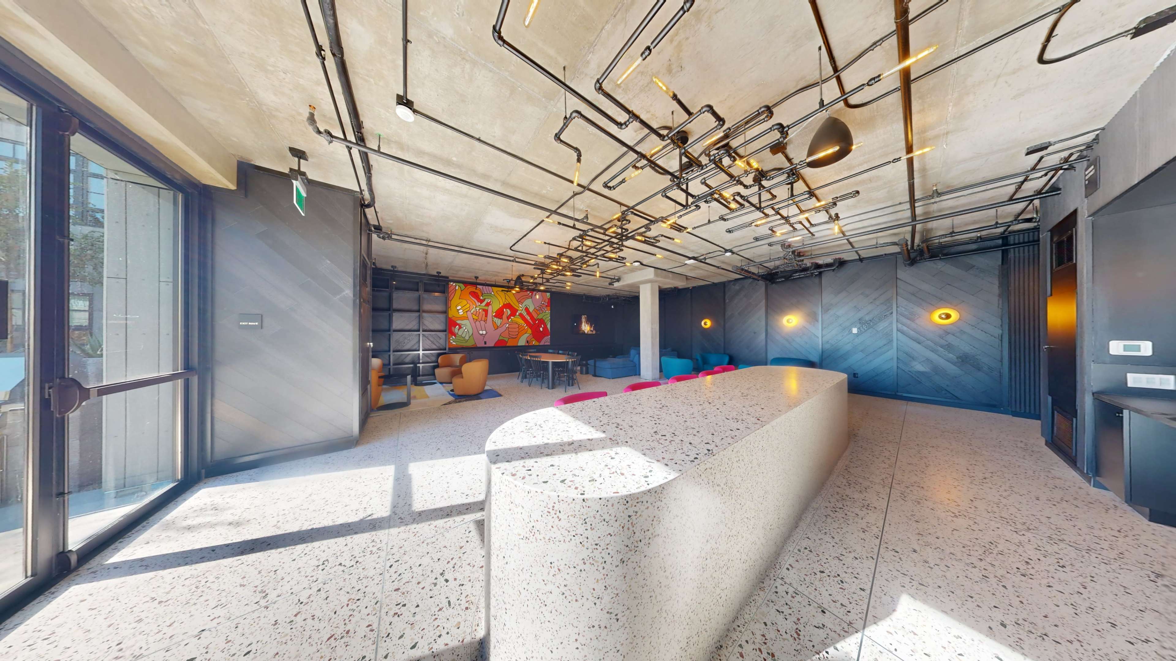 A modern interior space features a curved counter, colorful seating, and exposed light fixtures against a backdrop of industrial design elements.