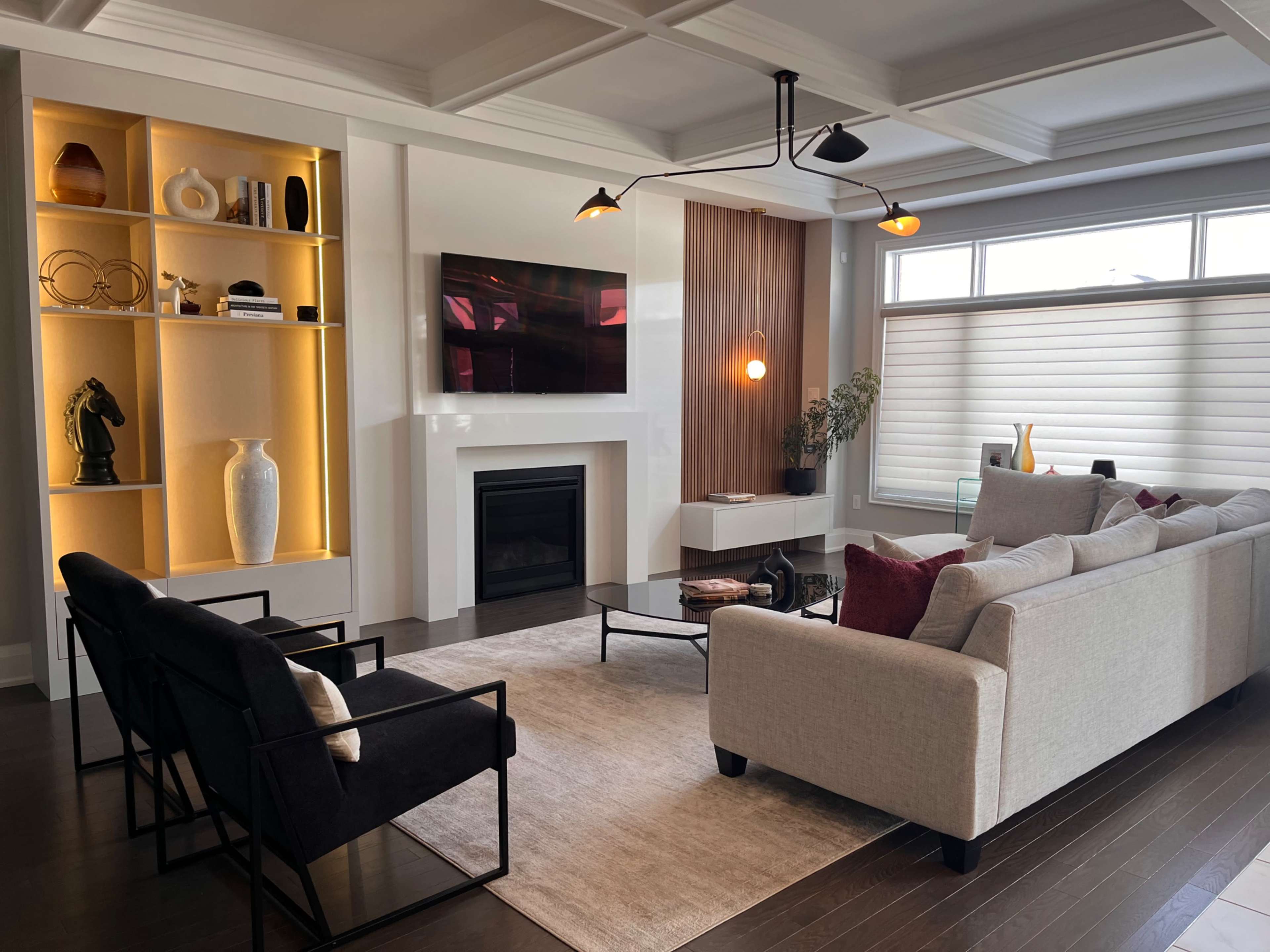 The image shows a modern living room with a light-colored sectional sofa, black accent chairs, a fireplace, and built-in shelving with decorative items.