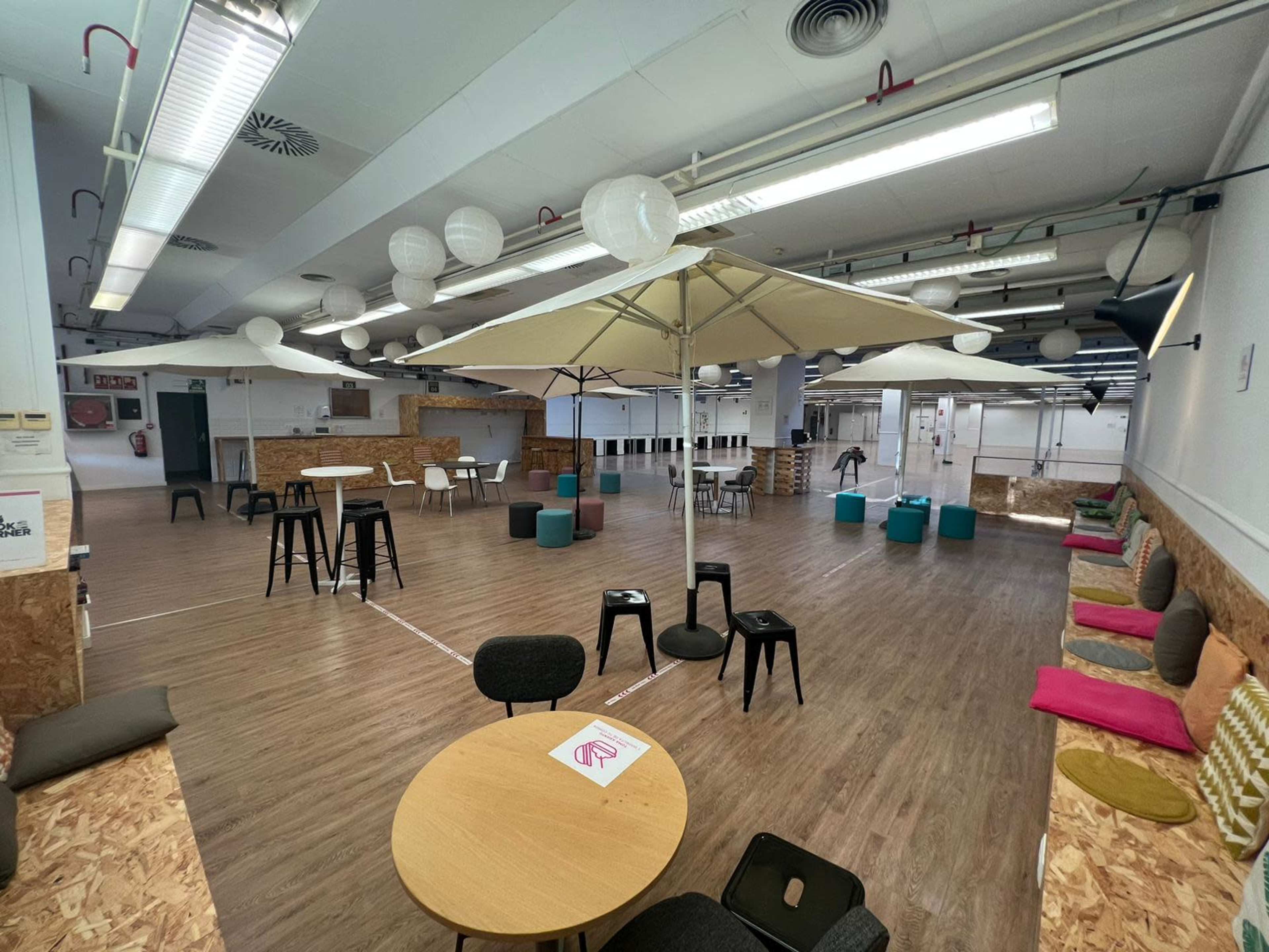 A spacious indoor area with tables, chairs, and umbrellas, featuring a mix of seating arrangements and colorful cushions.