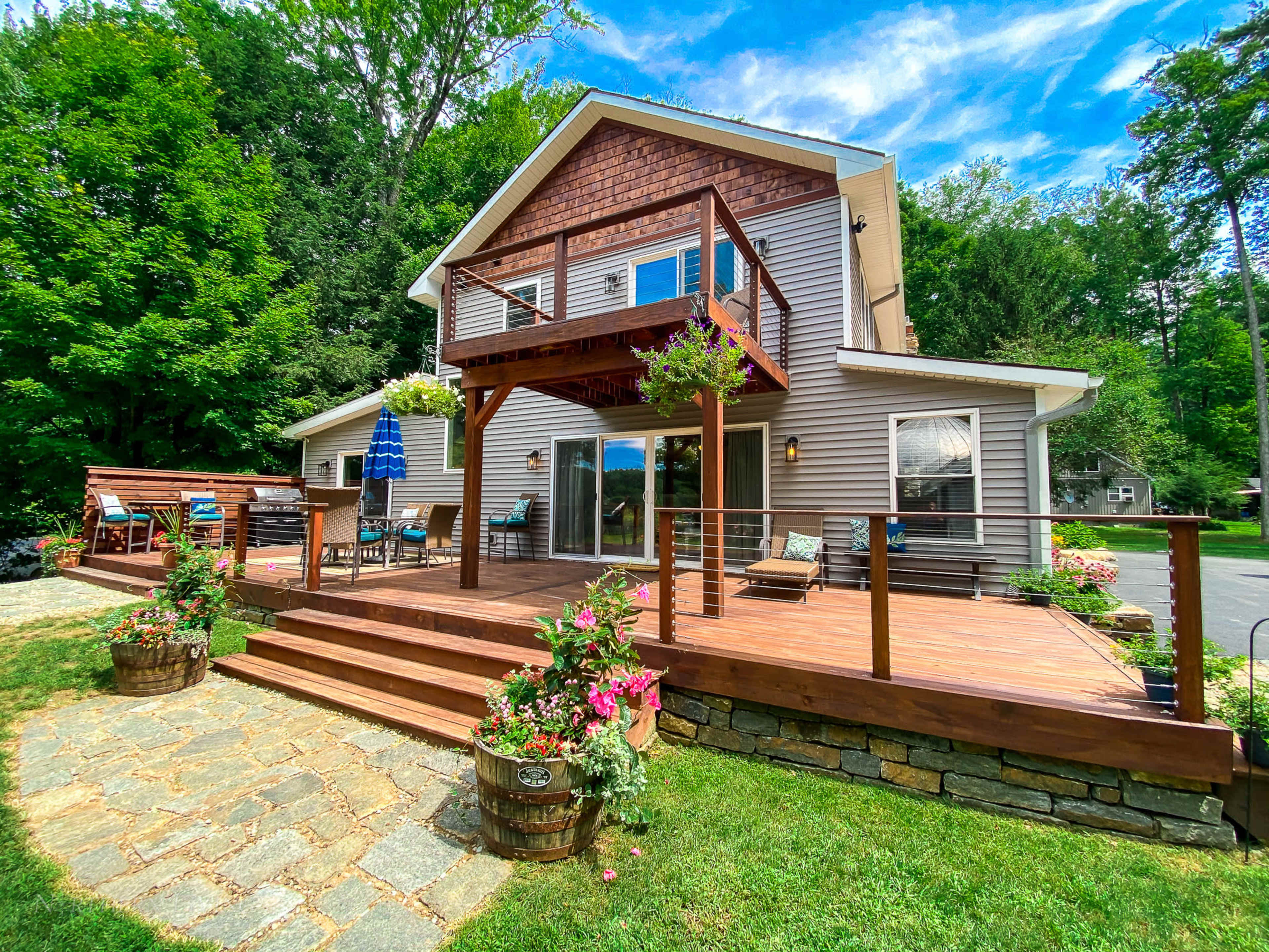 A two-story house with a wooden deck and a landscaped yard featuring stone pathways and flowerpots.