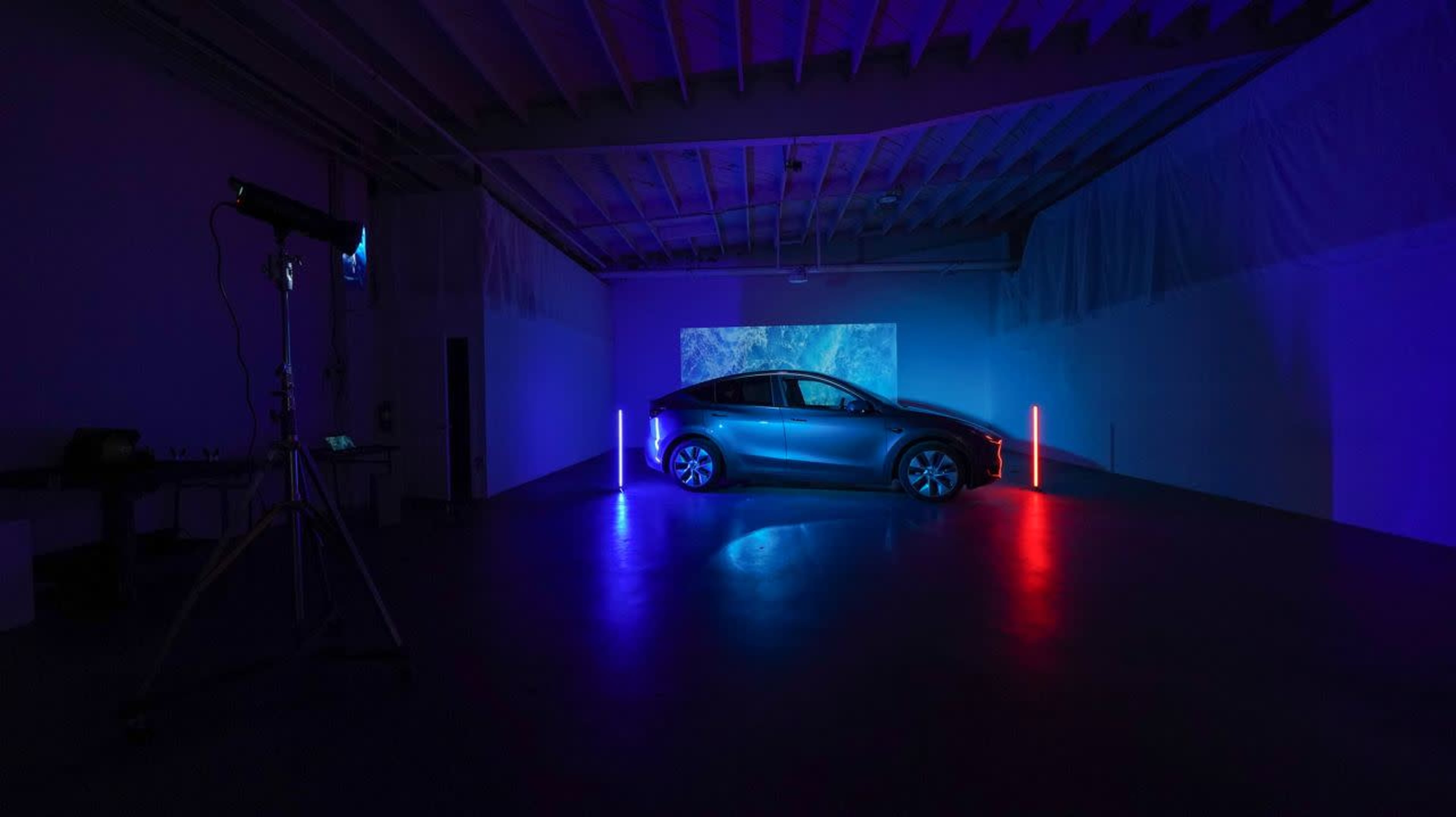 A car is positioned in a dimly lit room with colorful lighting and a projected image on the wall behind it.