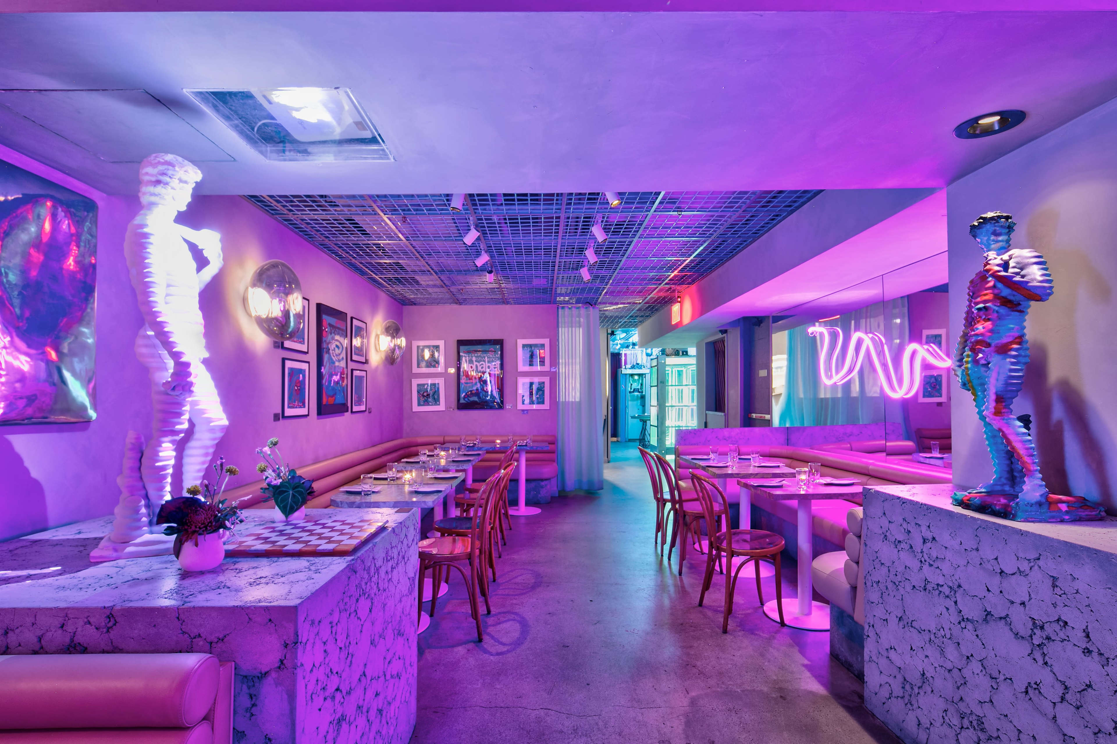 The image shows a modern restaurant interior with pink lighting, marble tables, and artistic statues positioned throughout the space.