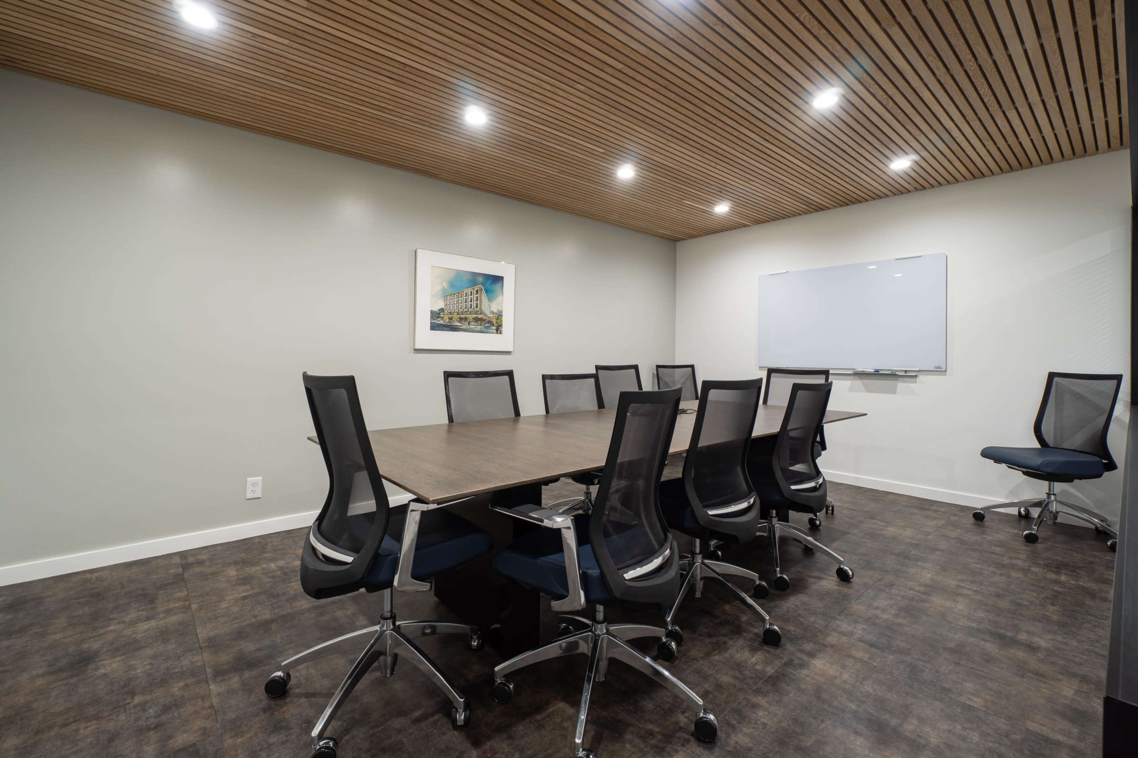 A modern conference room features a long table surrounded by black ergonomic chairs and a whiteboard on the wall.