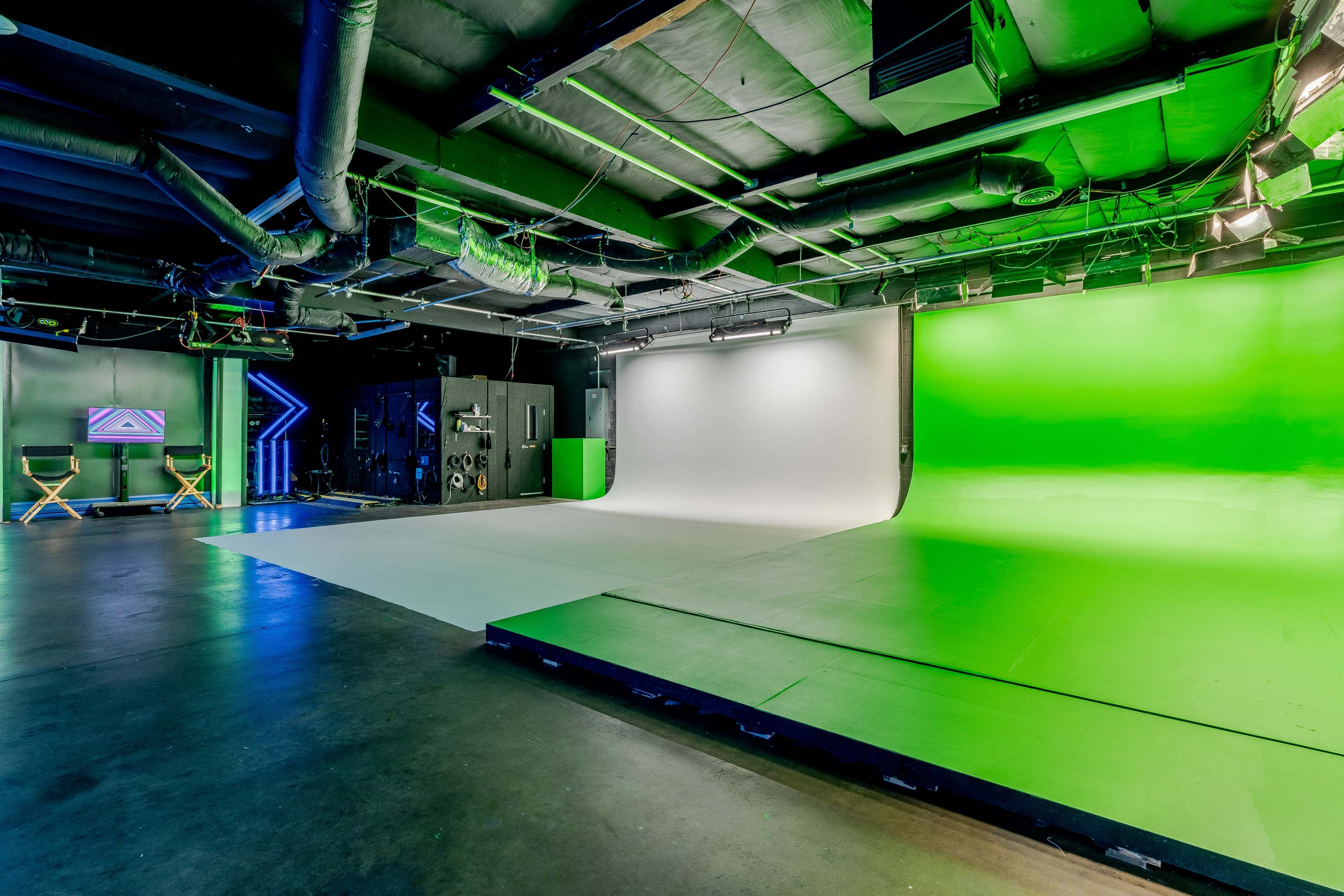 A modern studio space equipped with a green screen and a white backdrop, along with various lighting and equipment.